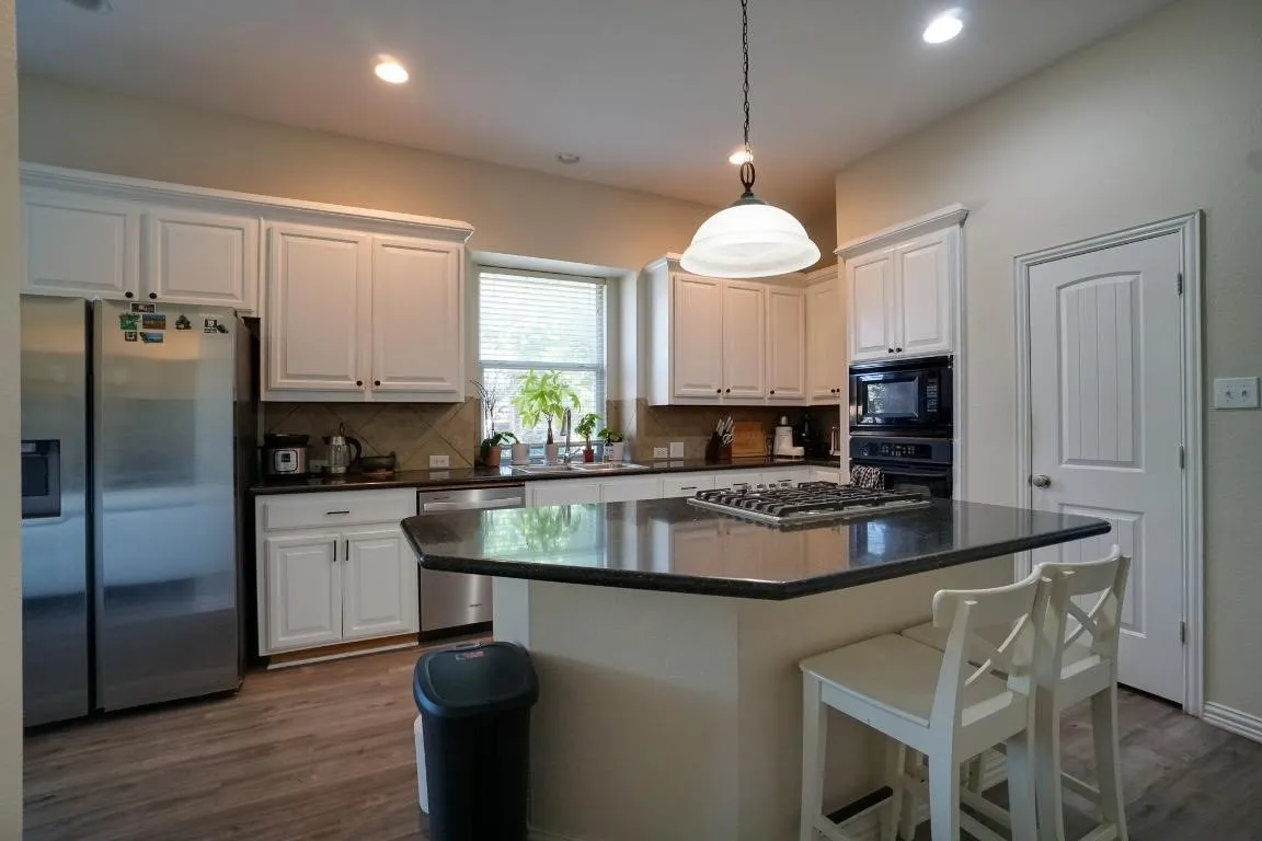 Kitchen featuring white cabinetry, dark countertops, wood-finish flooring, and a center island with a built-in gas cooktop