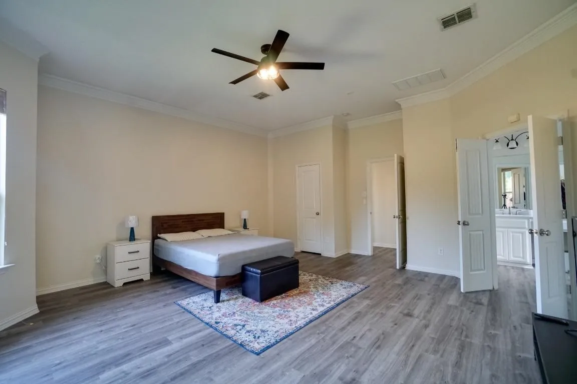 Expansive room featuring wood-finish flooring, crown molding, and a ceiling fan