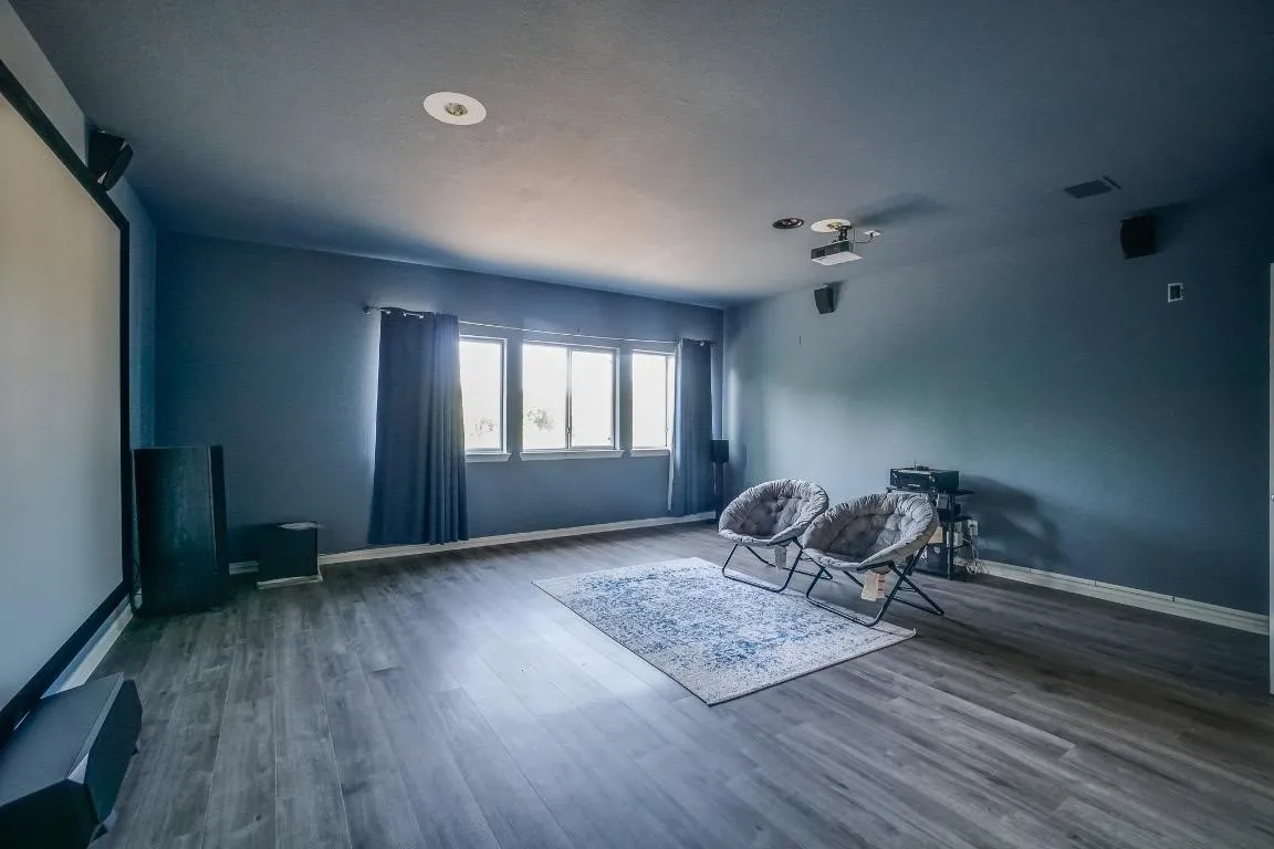 Spacious room featuring wood-finish flooring, multiple windows, a ceiling-mounted projector, and integrated ceiling speakers