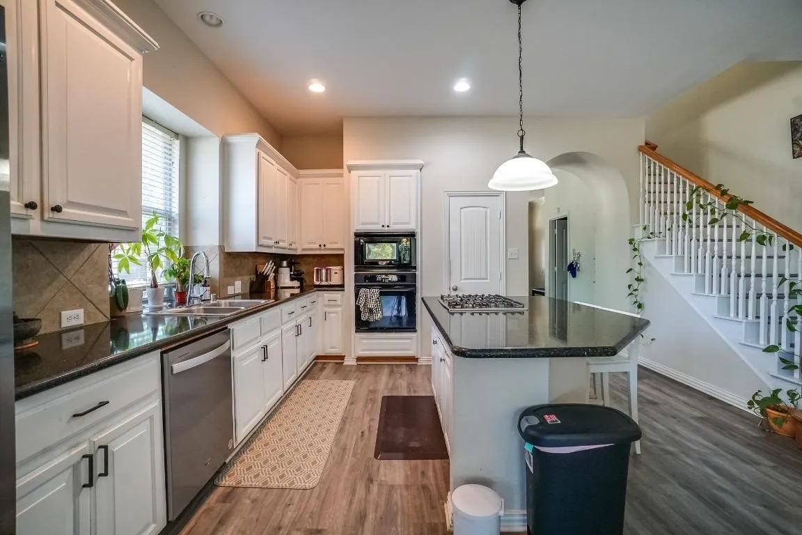 Kitchen featuring white cabinetry, dark countertops, stainless steel appliances, and wood-finish flooring