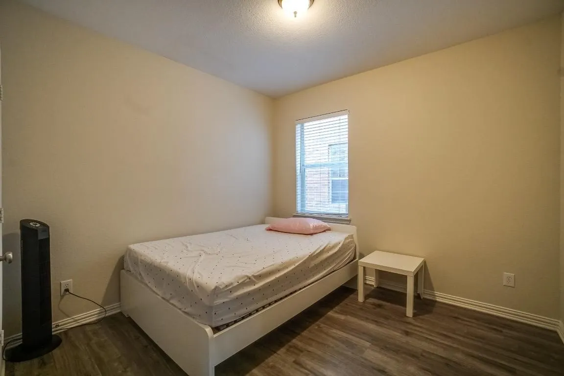 Wood-finish flooring, single window with blinds, ceiling-mounted light fixture, light-toned wall paint, and white trim