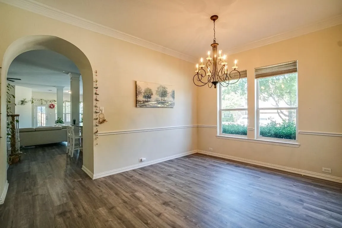 Wood-finish flooring, crown molding, wall paneling, and an arched entryway