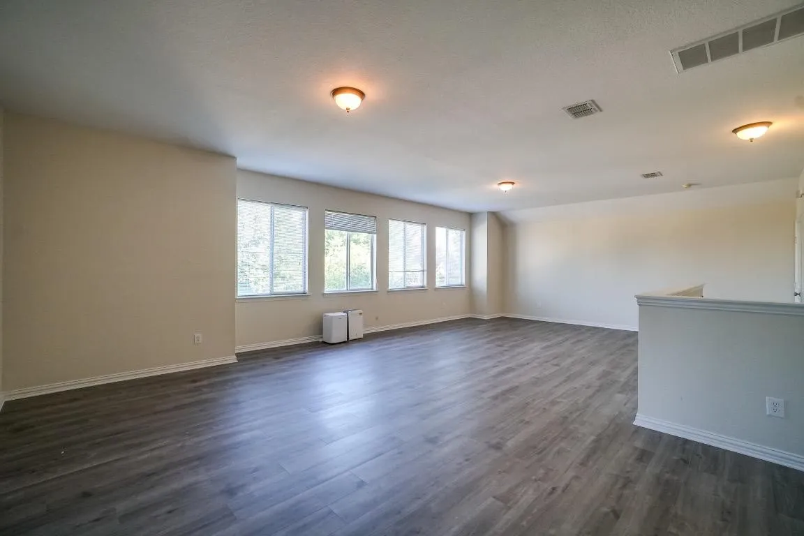 Spacious room with wood-finish flooring, multiple windows, and recessed lighting fixtures