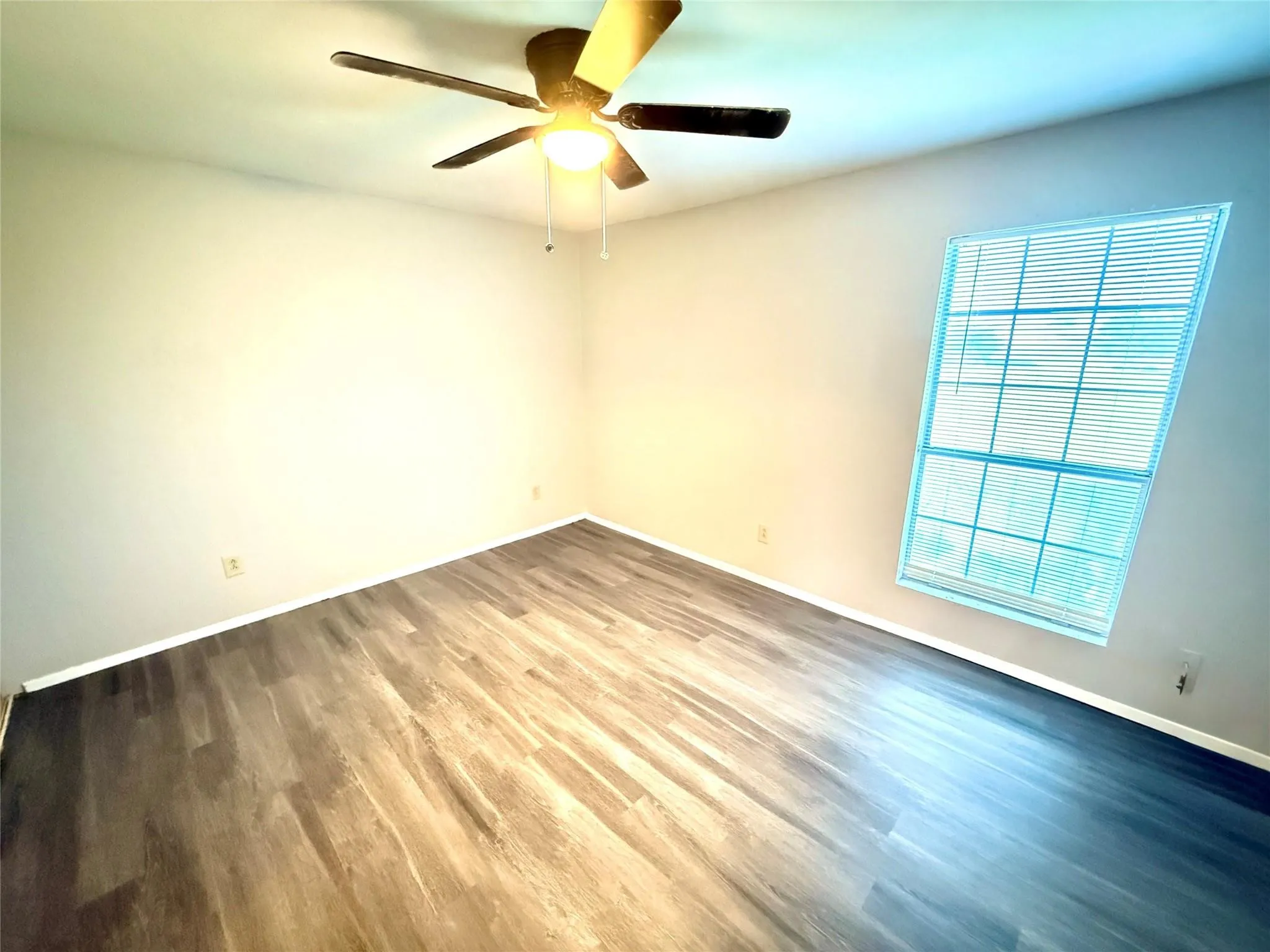 Wood-finish flooring, ceiling fan with integrated lighting, and a window with blinds
