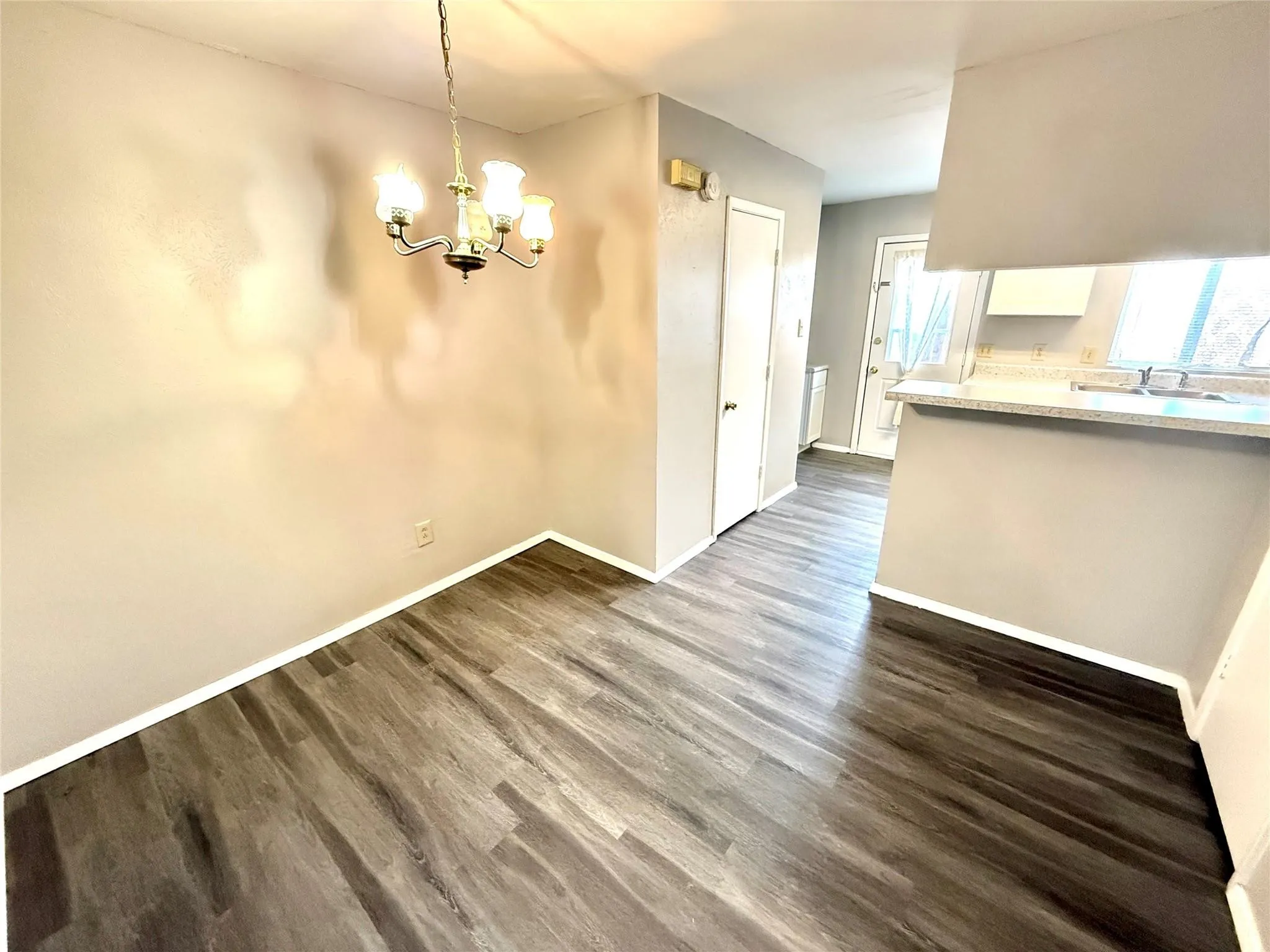 Dining area featuring wood-finish flooring, a four-light chandelier, and access to the kitchen with a serving bar and solid surface countertops