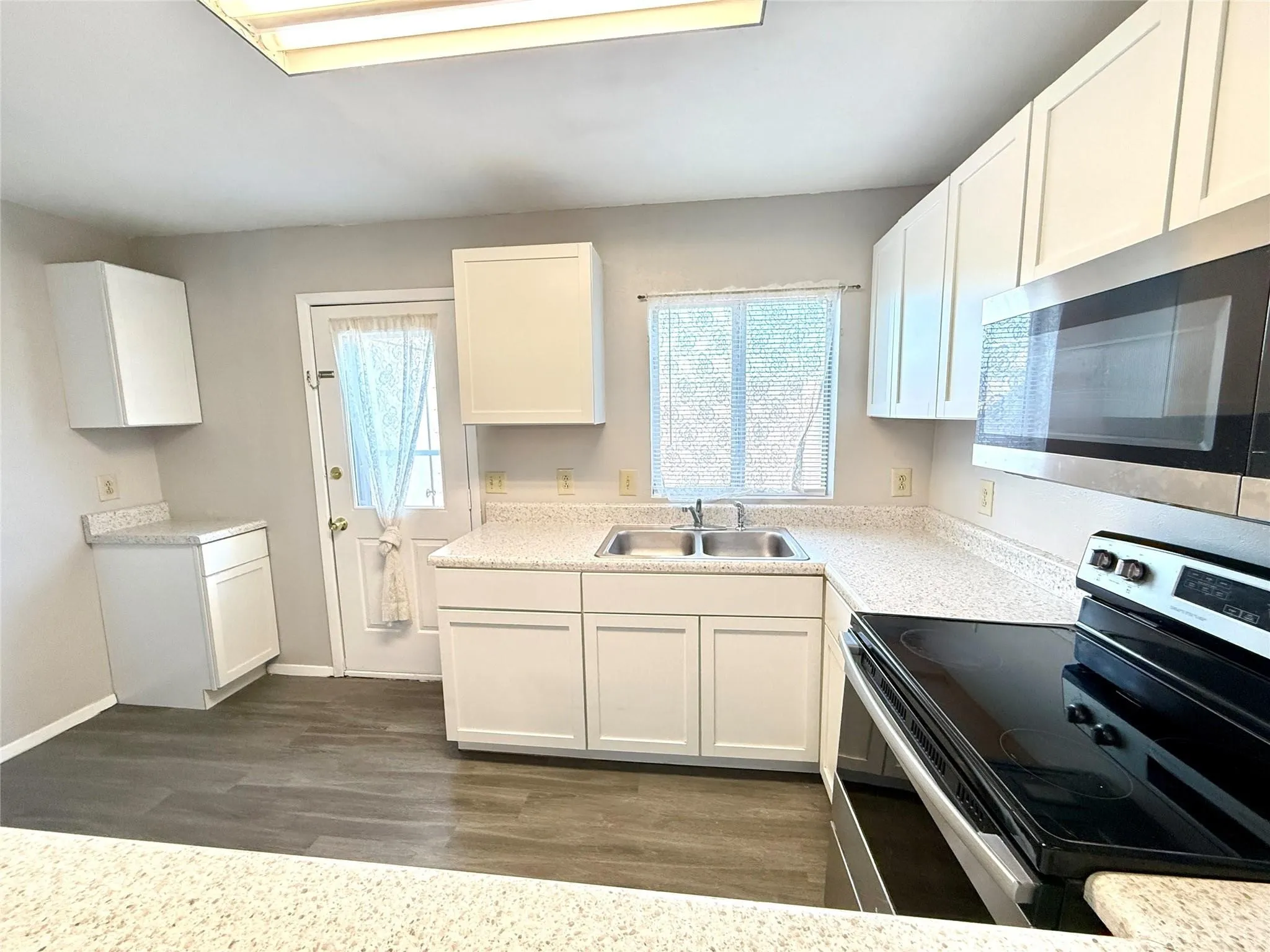 Wood-finish flooring, white cabinetry, integrated stainless steel microwave, stainless steel sink, and light-toned countertops