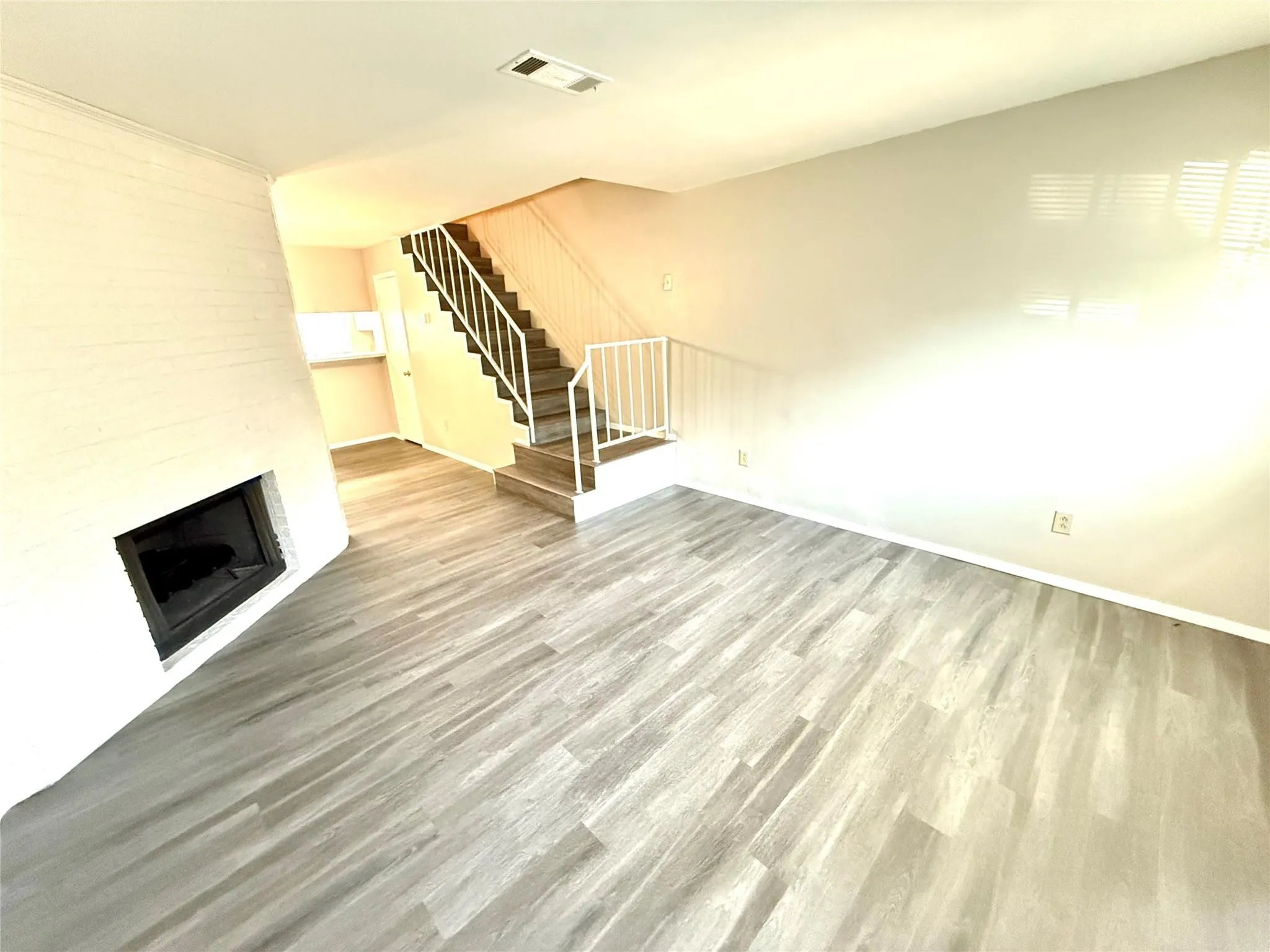 Living area featuring wood-finish flooring, a white brick fireplace, and an open staircase with white railings
