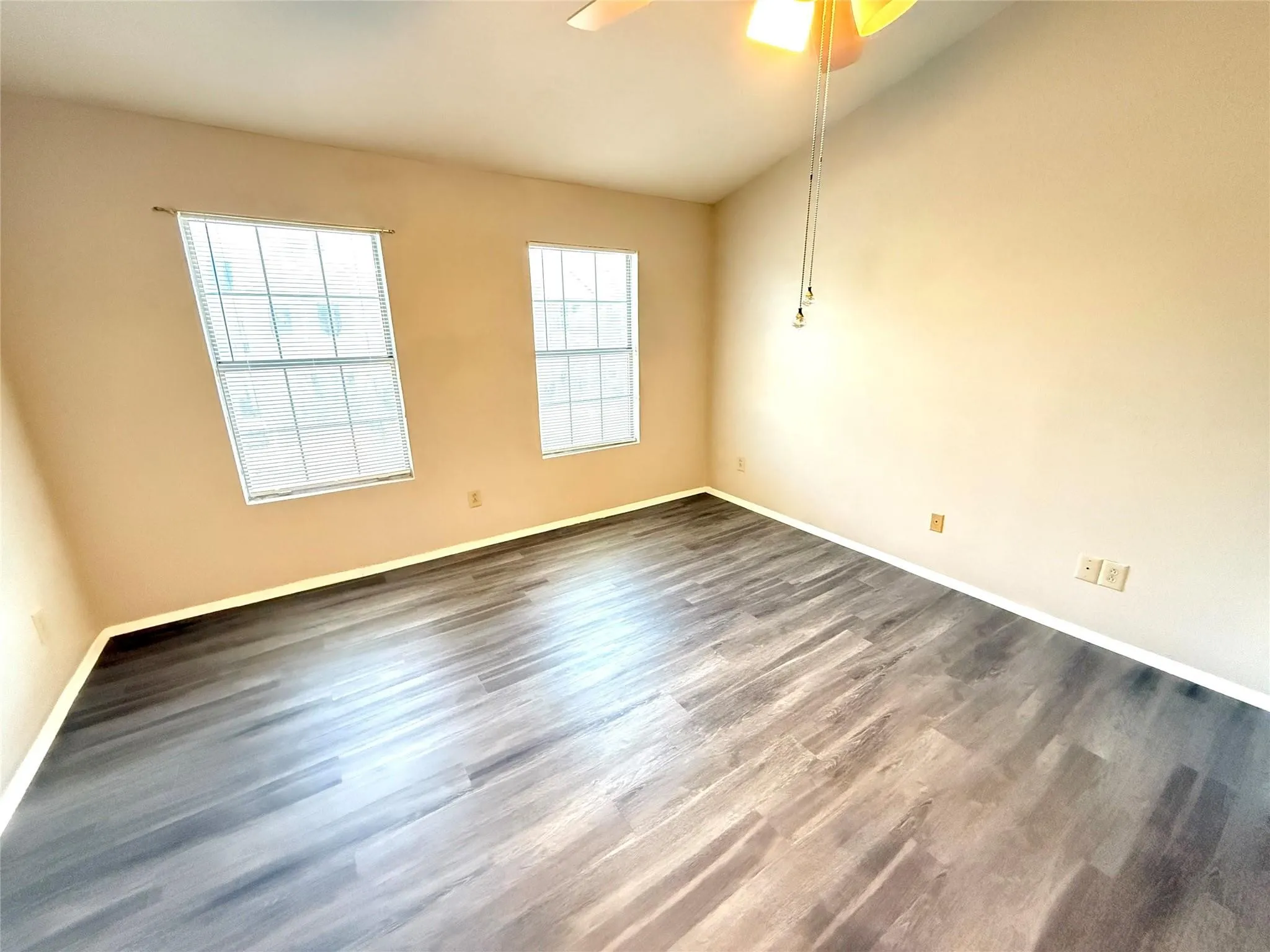Wood-finish flooring, two large windows with blinds, ceiling fan with integrated lighting, and neutral wall tones