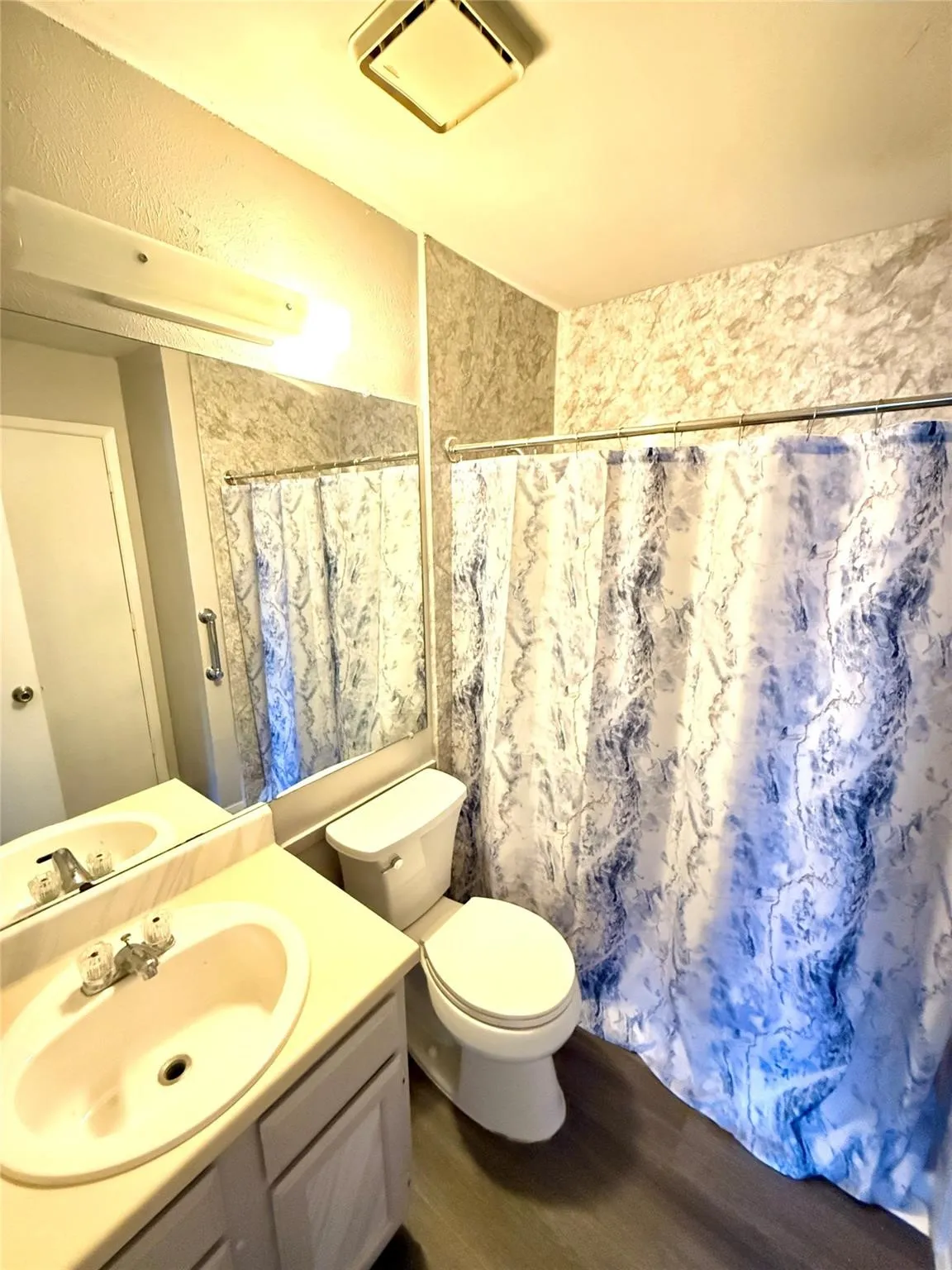 Bathroom featuring a vanity with an integrated sink, a toilet, a full-width mirror, and wood-finish flooring