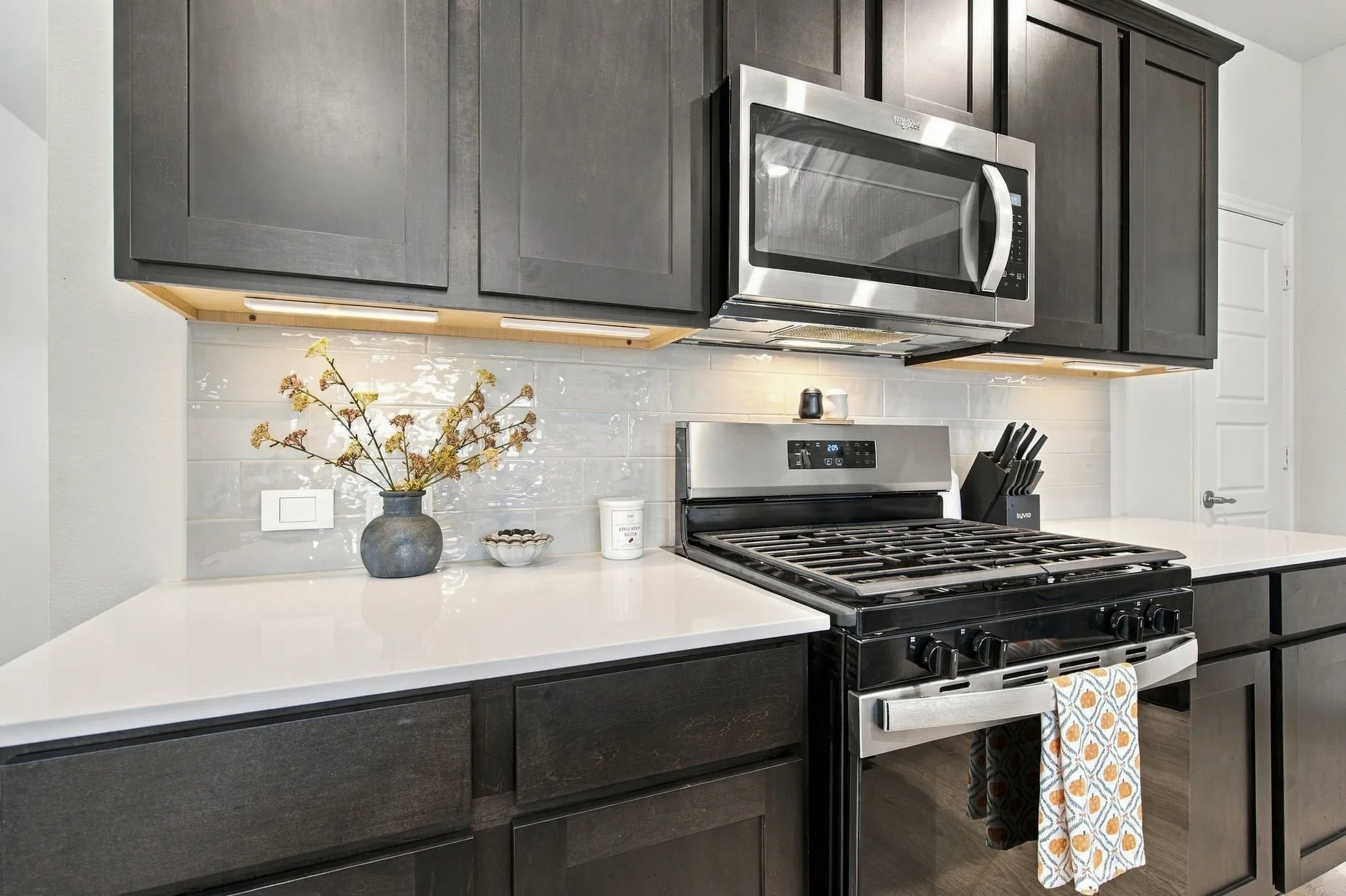 White subway tile backsplash, and under-cabinet lighting, and a gas range cooktop