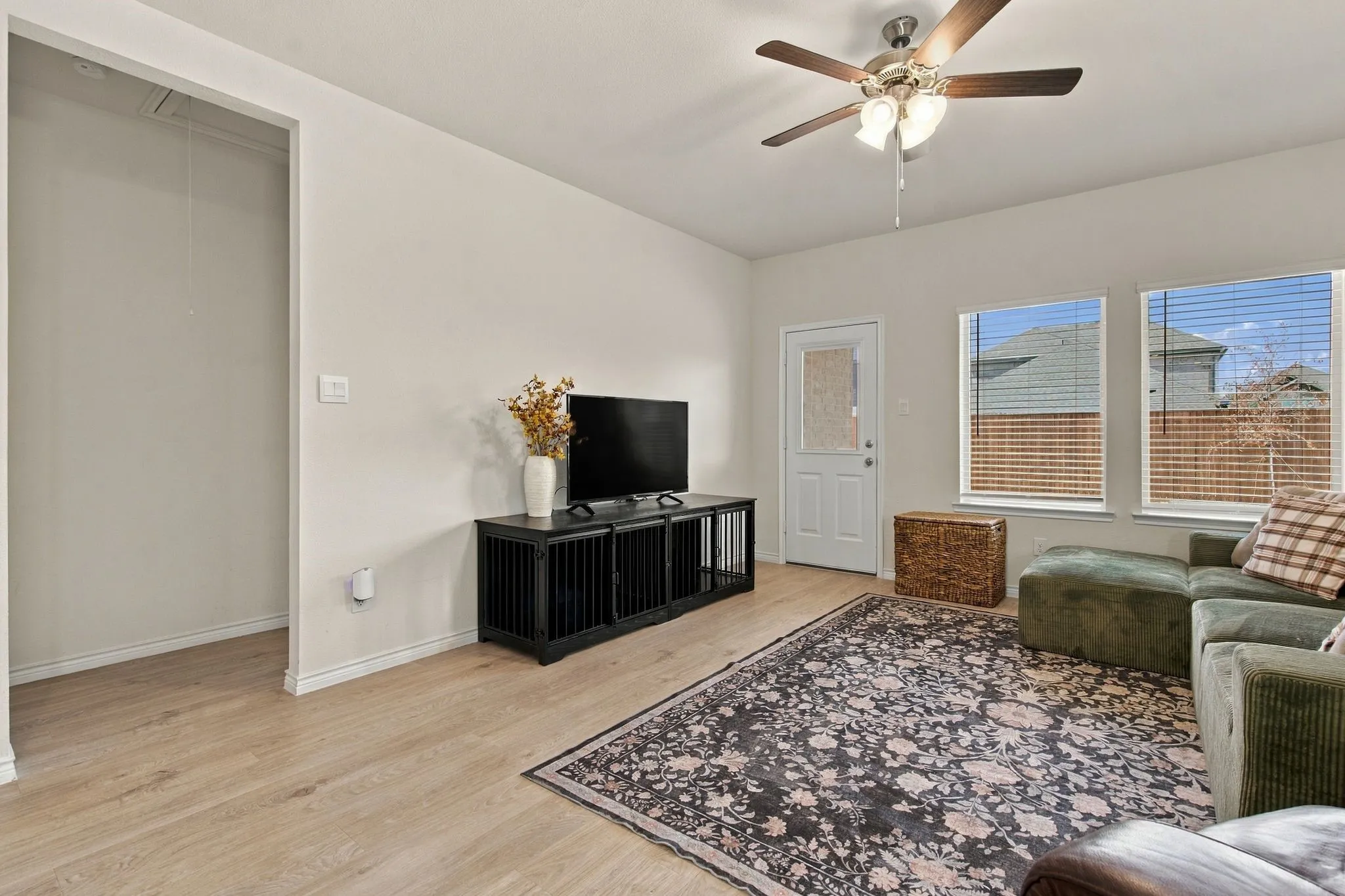 Light wood-finish flooring, multiple windows with blinds, ceiling fan with integrated lighting, recessed entryway, and a solid exterior door with a glass insert