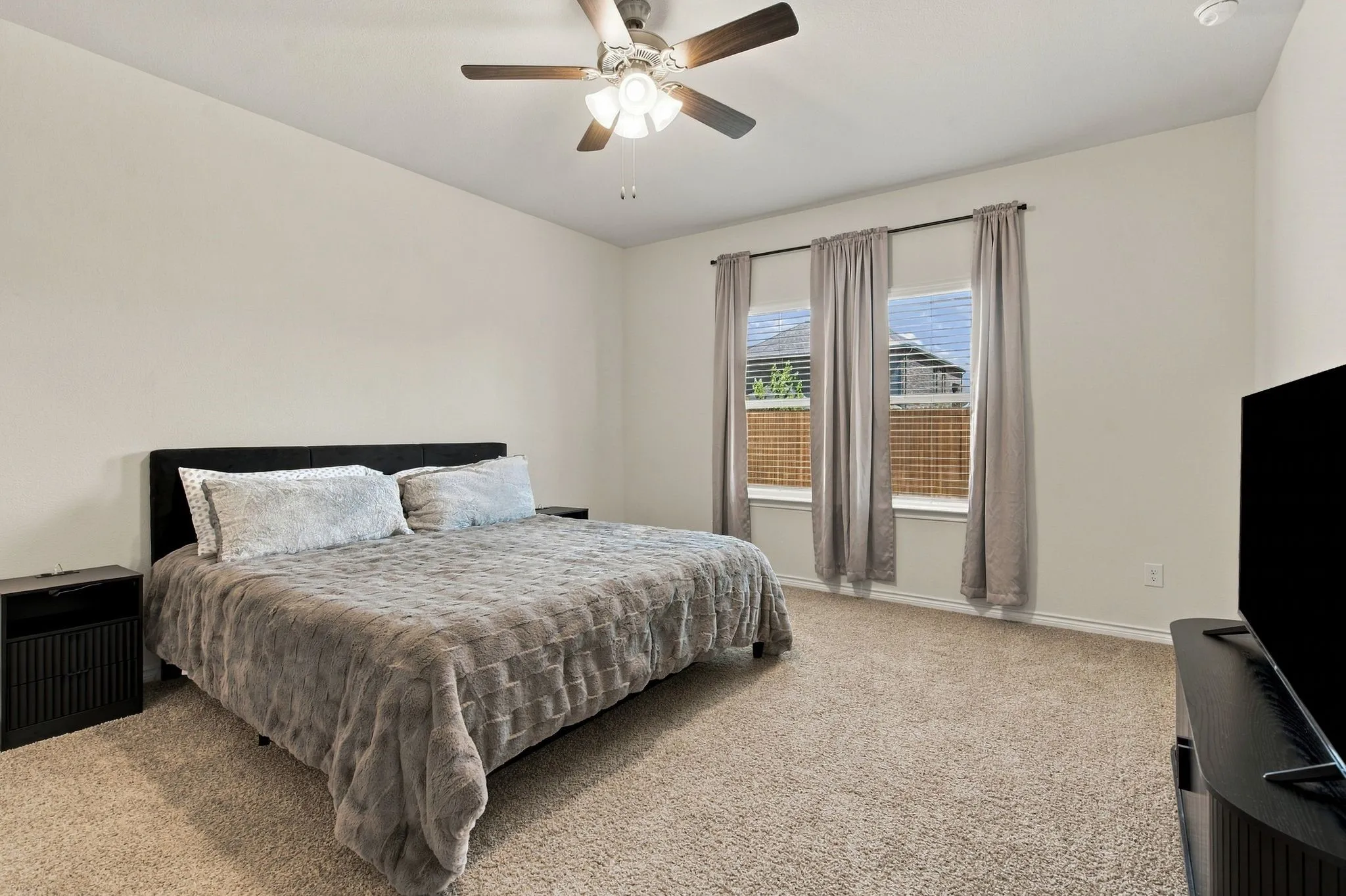 Neutral tone wall paint, light neutral carpet, two windows with blinds, and a ceiling fan with integrated lighting and ensuite primary bath