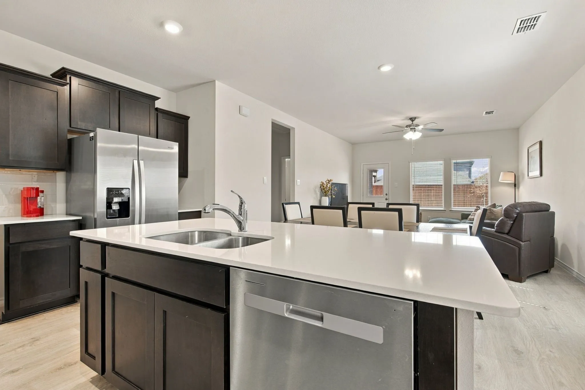 Kitchen island with integrated stainless steel sink and dishwasher, white countertops, dark wood cabinetry, and recessed lighting