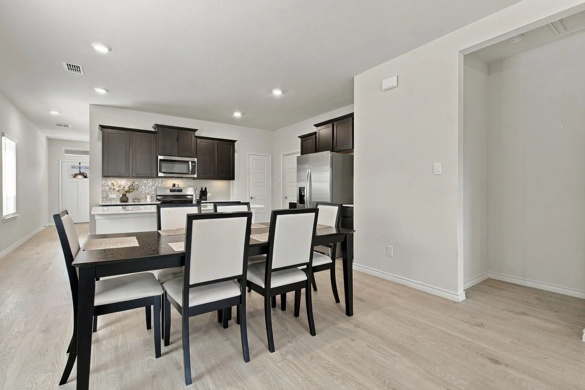 Open-concept dining area featuring wood-finish flooring, recessed lighting, and a kitchen with dark cabinetry and stainless steel appliances