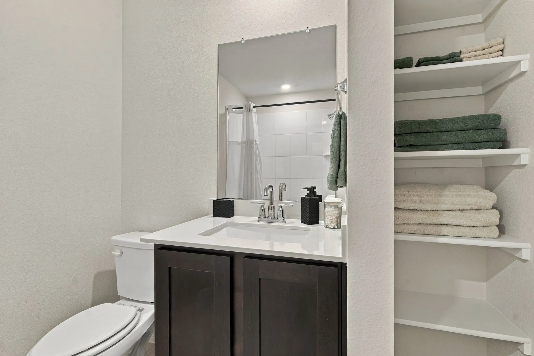 Built-in shelving, dark wood-finish vanity, white countertop, integrated sink, and a rectangular mirror