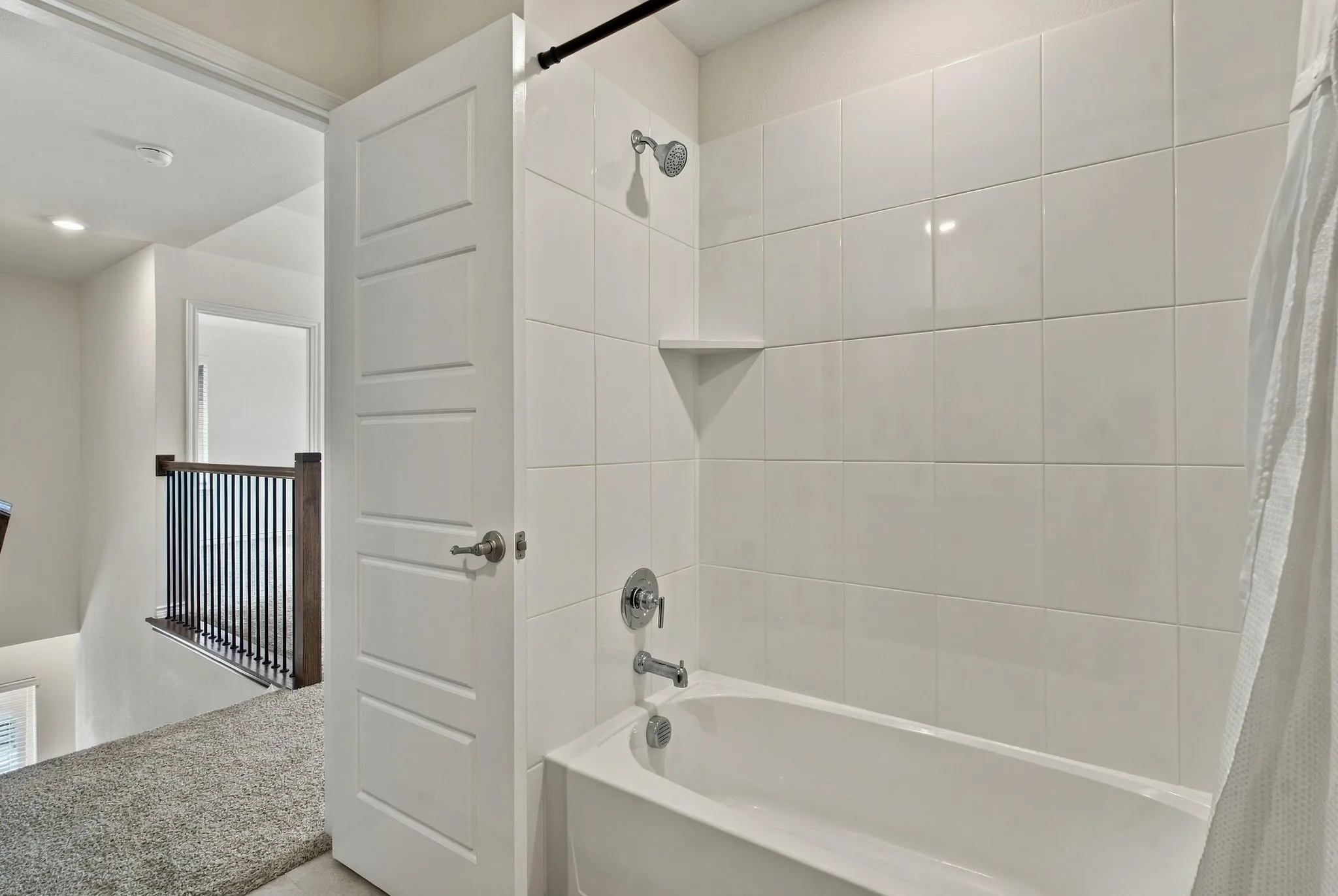 White tiled shower with a built-in shelf, chrome fixtures, and an integrated tub