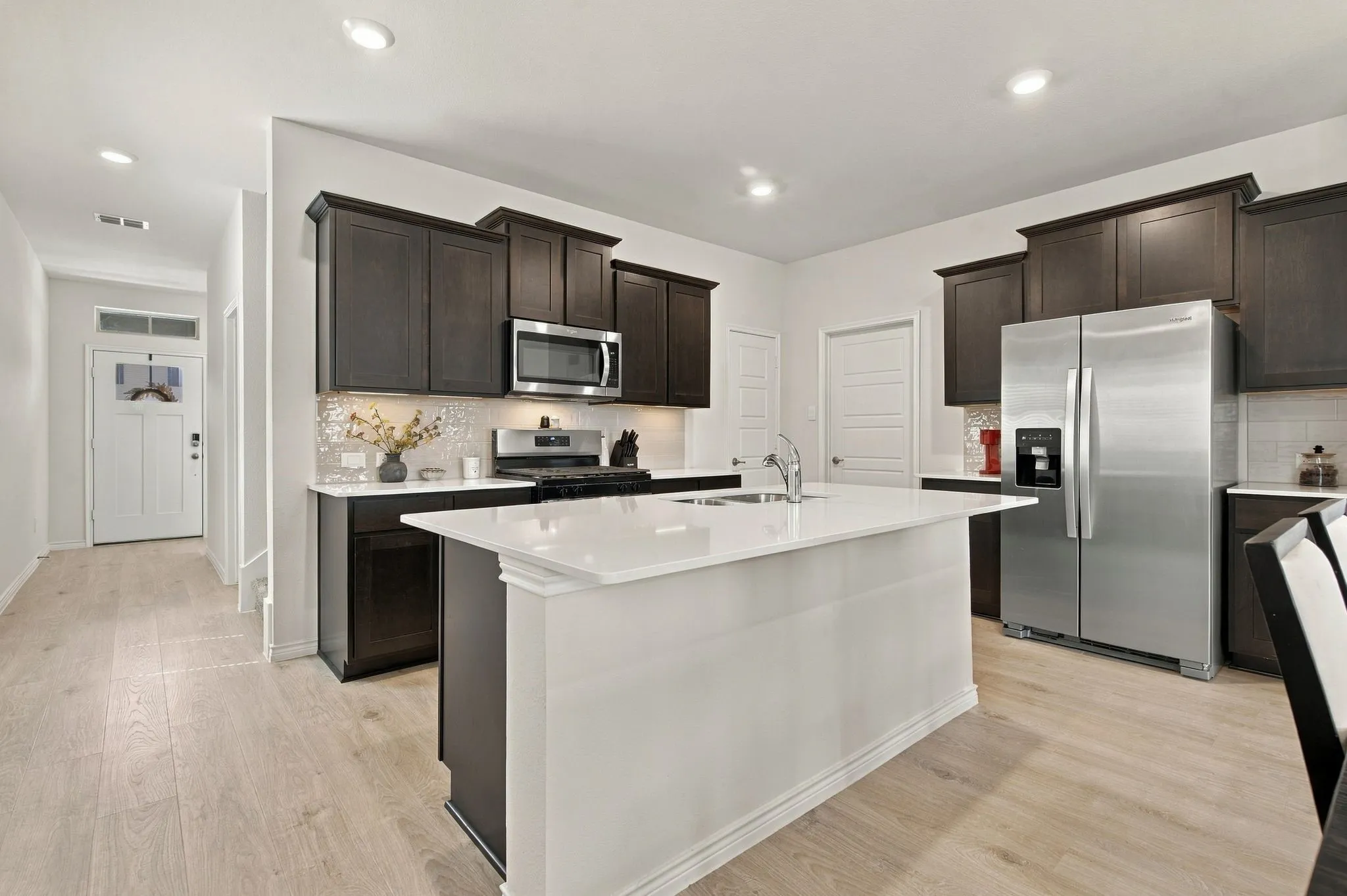 Kitchen featuring an island with a white countertop, stainless steel appliances, dark wood cabinetry, and light wood-finish flooring