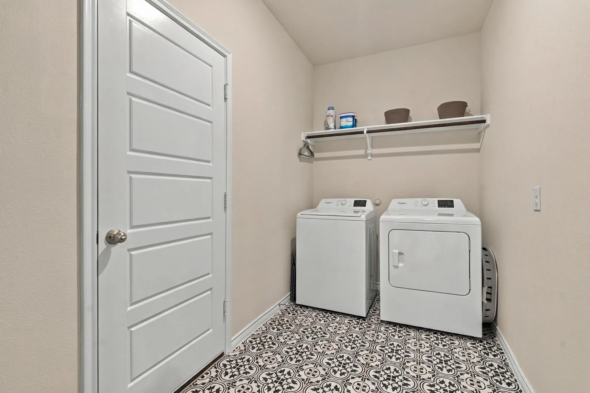 Laundry area with decorative floor tiling, an upper storage shelf, and a four-panel interior door to garage