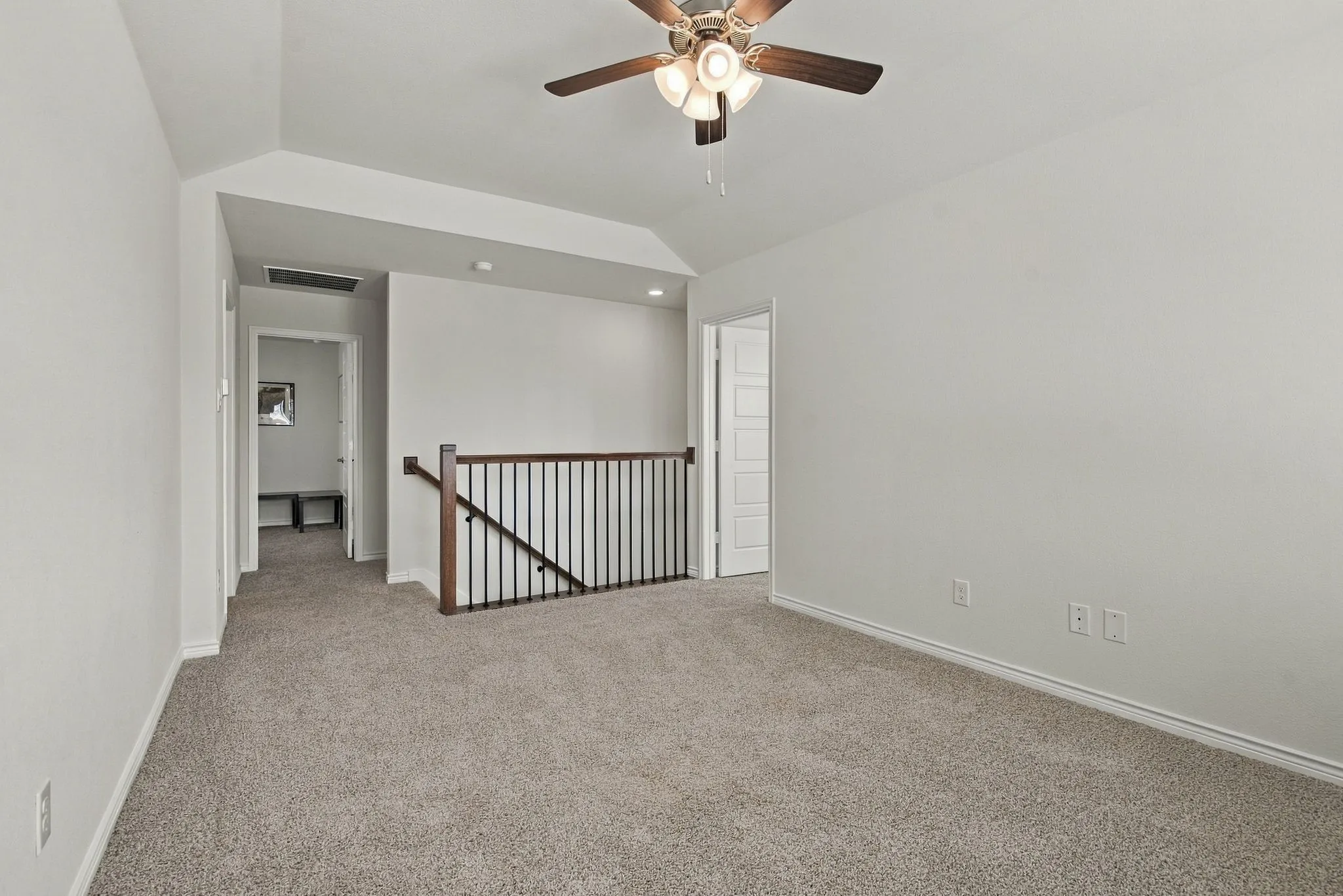 Vaulted ceiling with a ceiling fan, carpeted flooring, white walls, and a wood and metal stair railing
