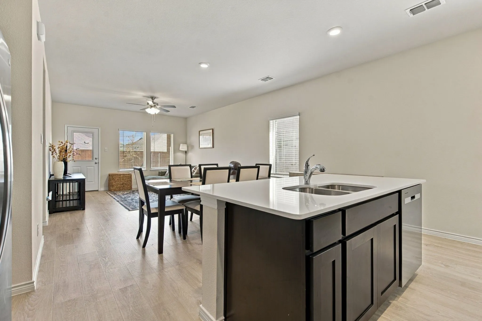 Kitchen island with a double basin stainless steel sink, dark wood-finish cabinetry, and a light-toned countertop