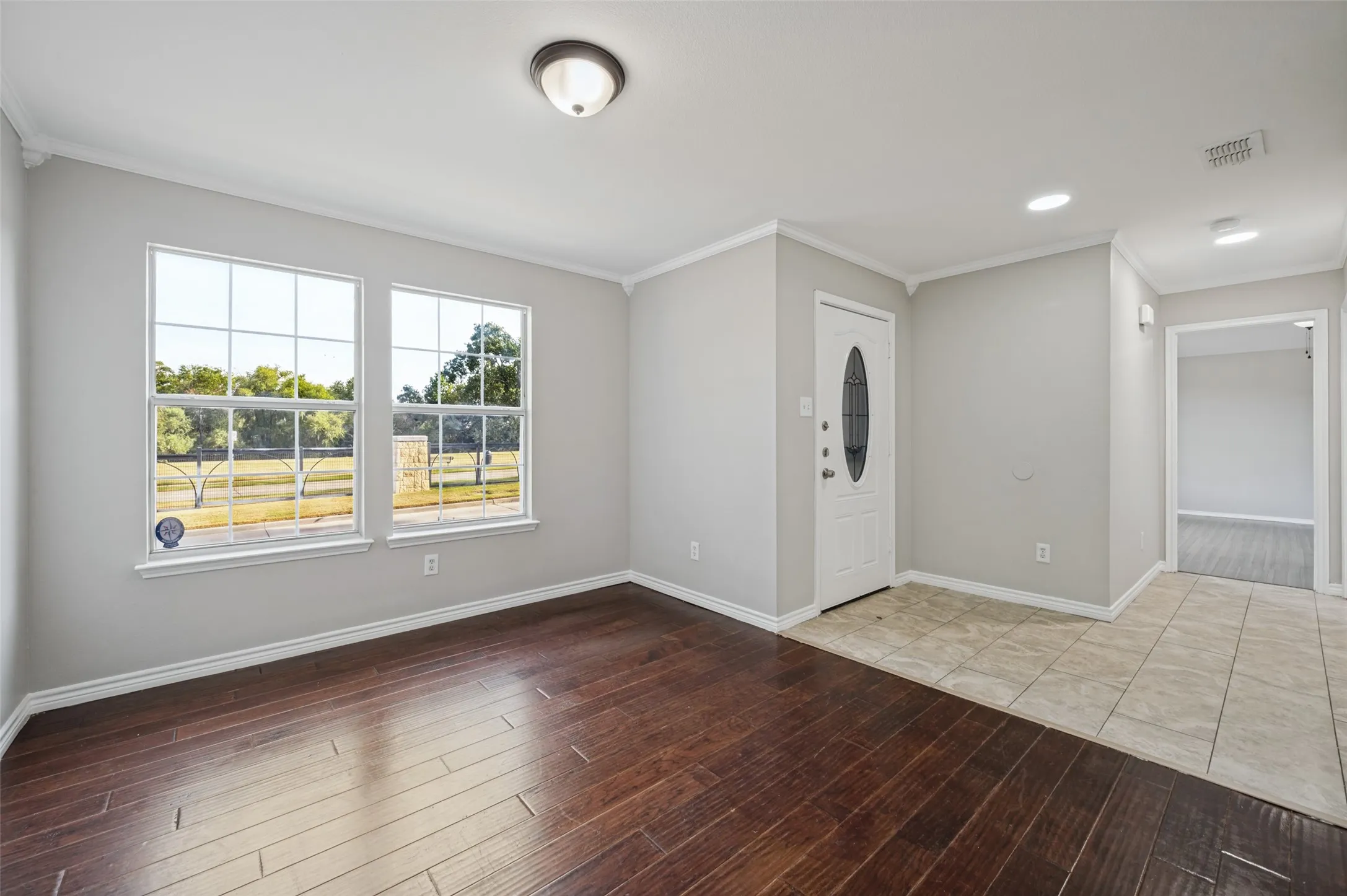 Entry area featuring wood-finish flooring, two large windows, a white paneled door with an oval-shaped glass insert, and neutral wall paint