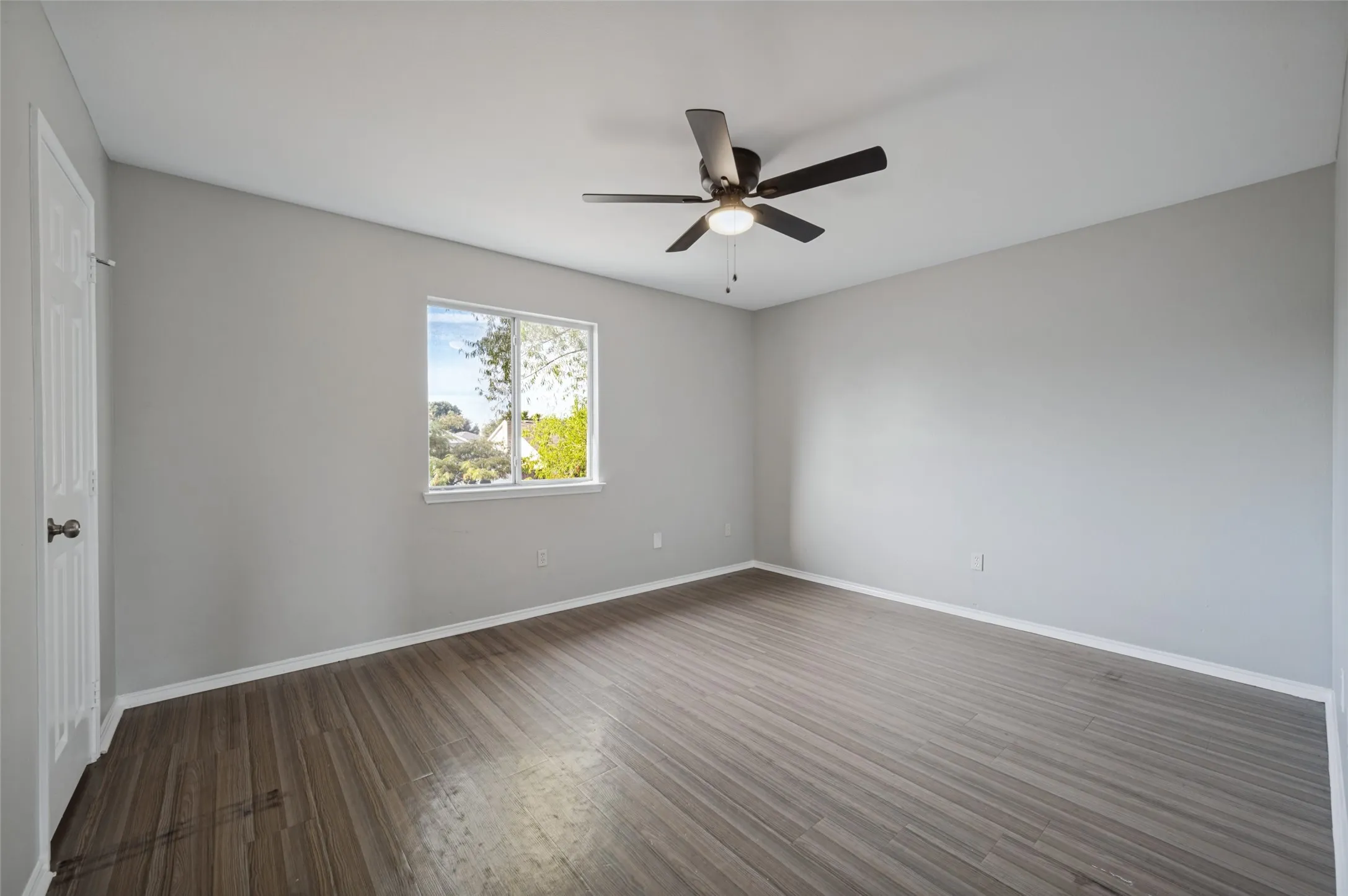 Spacious room with wood-finish flooring, a contemporary ceiling fan, and a single window providing natural light