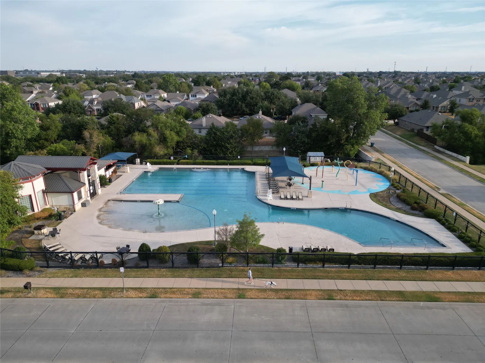 Expansive community pool complex featuring a multi-lane swimming pool, a separate recreation pool, a dedicated splash pad area, and an adjacent amenity building
