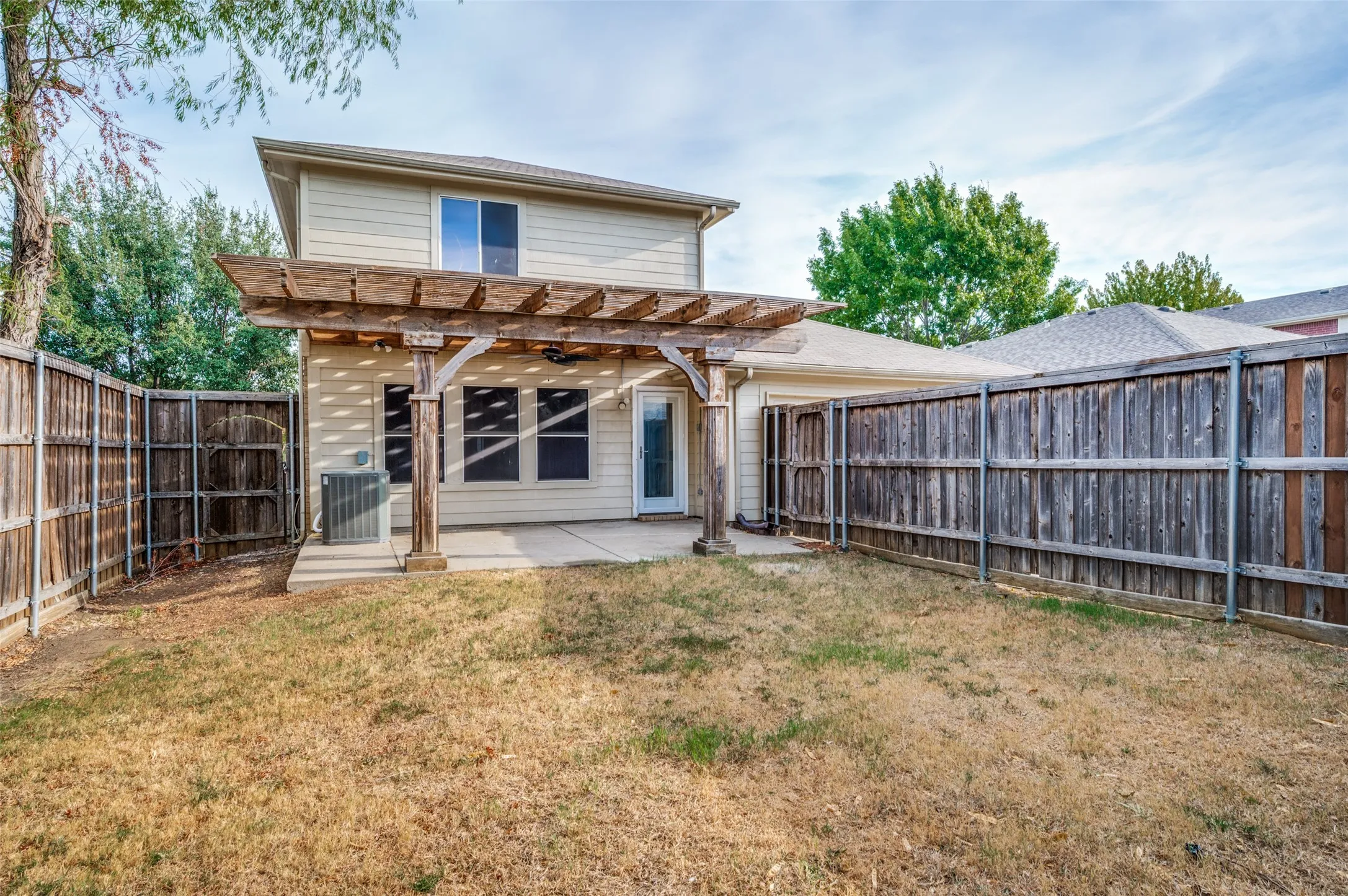 Rear exterior with an extensive yard, covered patio, and a wood pergola with built-in ceiling fan