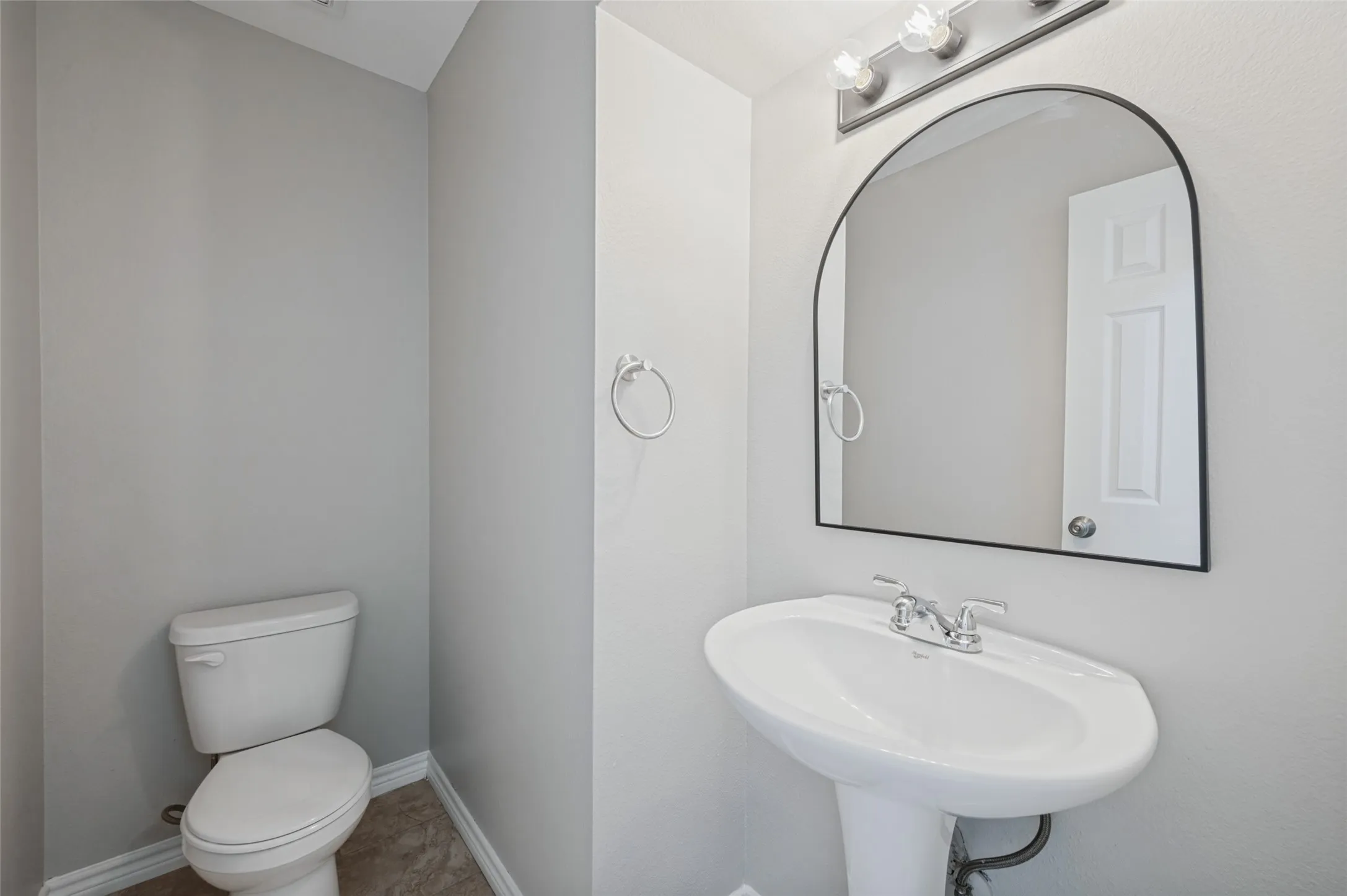 Pedestal sink with chrome fixtures, arched mirror, and vanity lighting