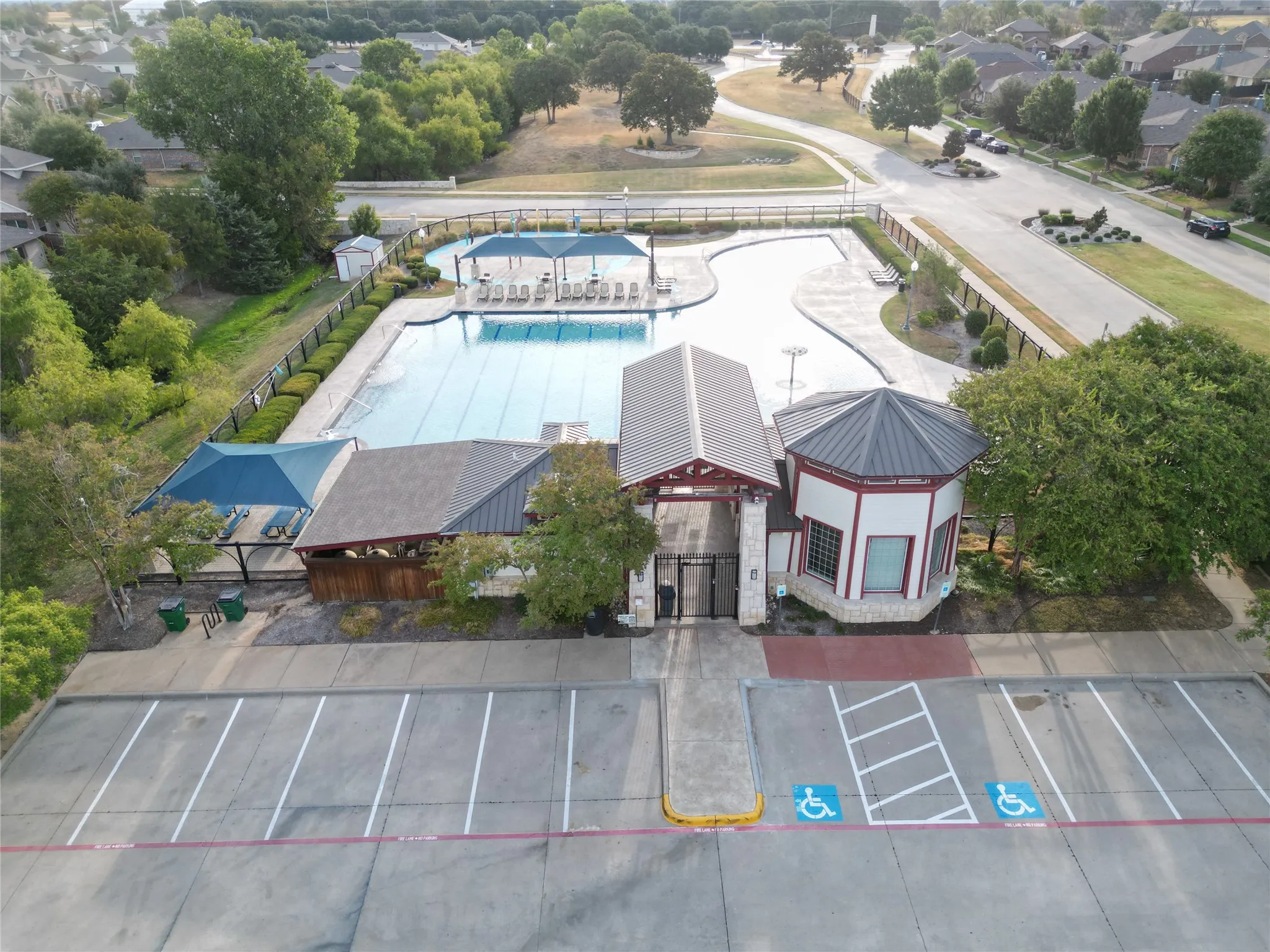 Community amenity center featuring a swimming pool, shaded lounge areas, and an adjacent parking lot