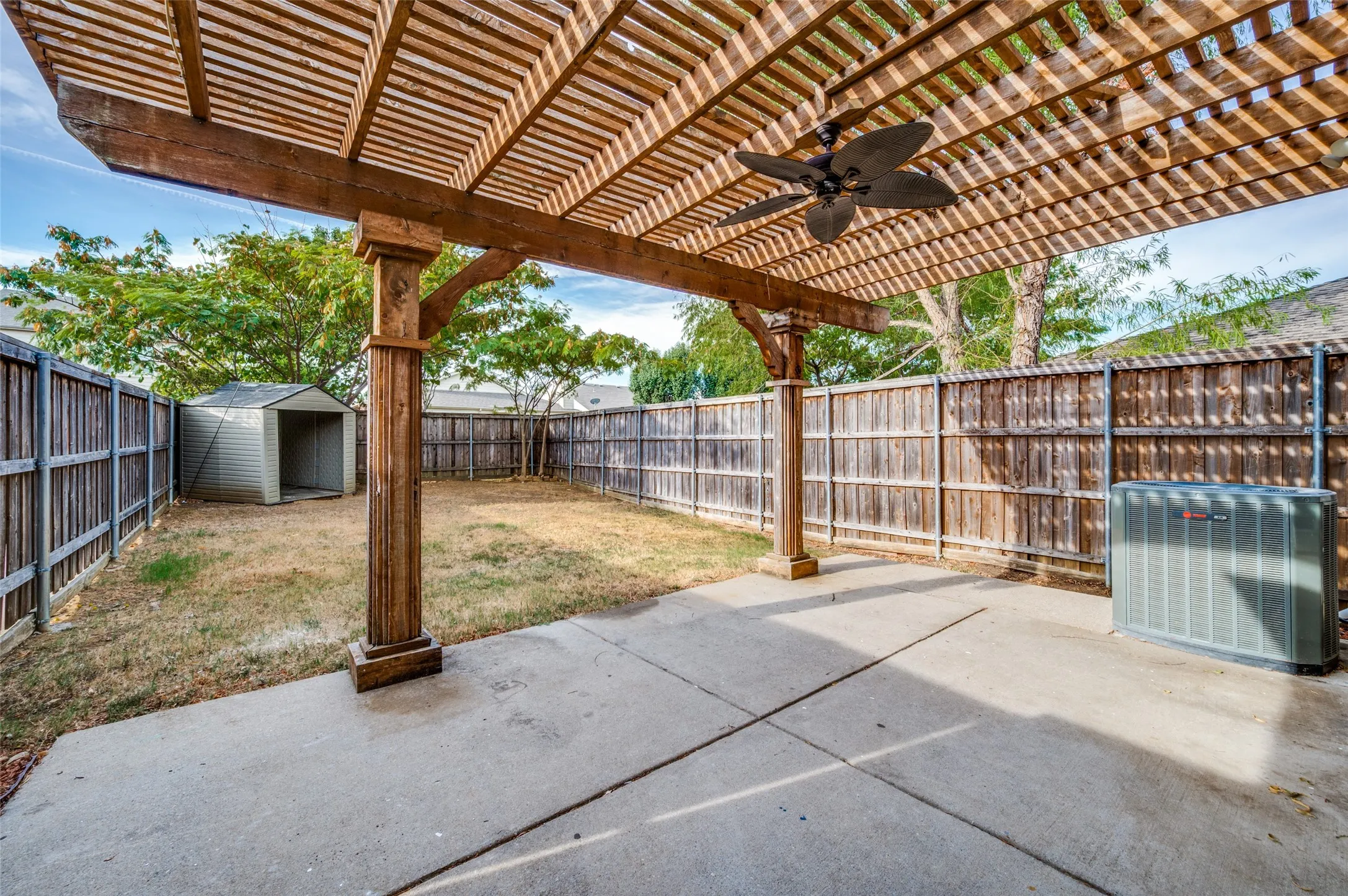 Concrete patio with a wood-slat pergola, integrated ceiling fan, and fenced perimeter