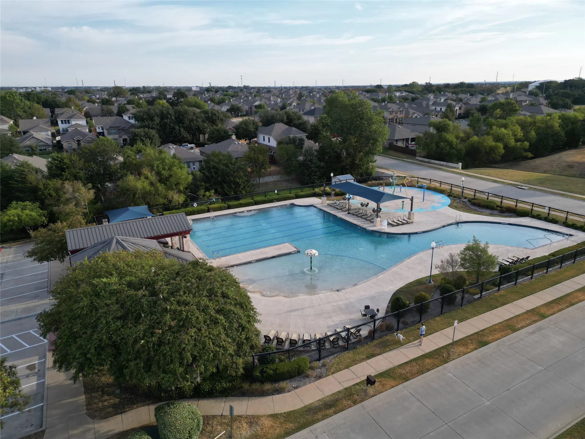 Expansive community pool with multiple swimming areas, a large shade structure, and surrounding hardscaping