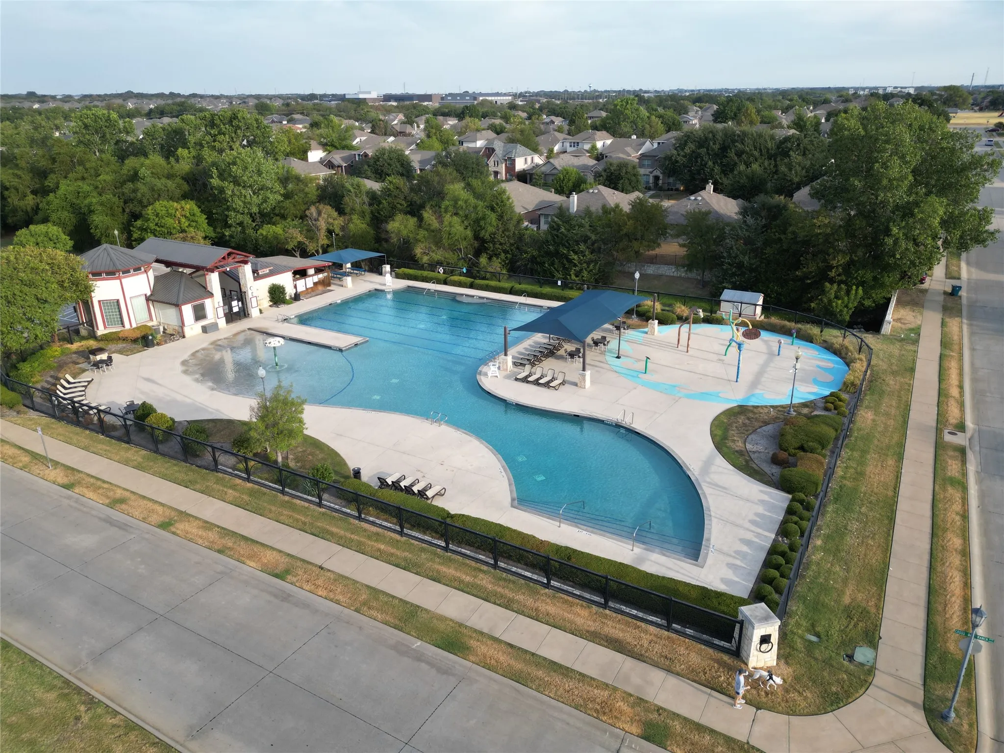 Resort-style pool area featuring multiple swimming zones, an integrated splash pad, and a shaded lounge area