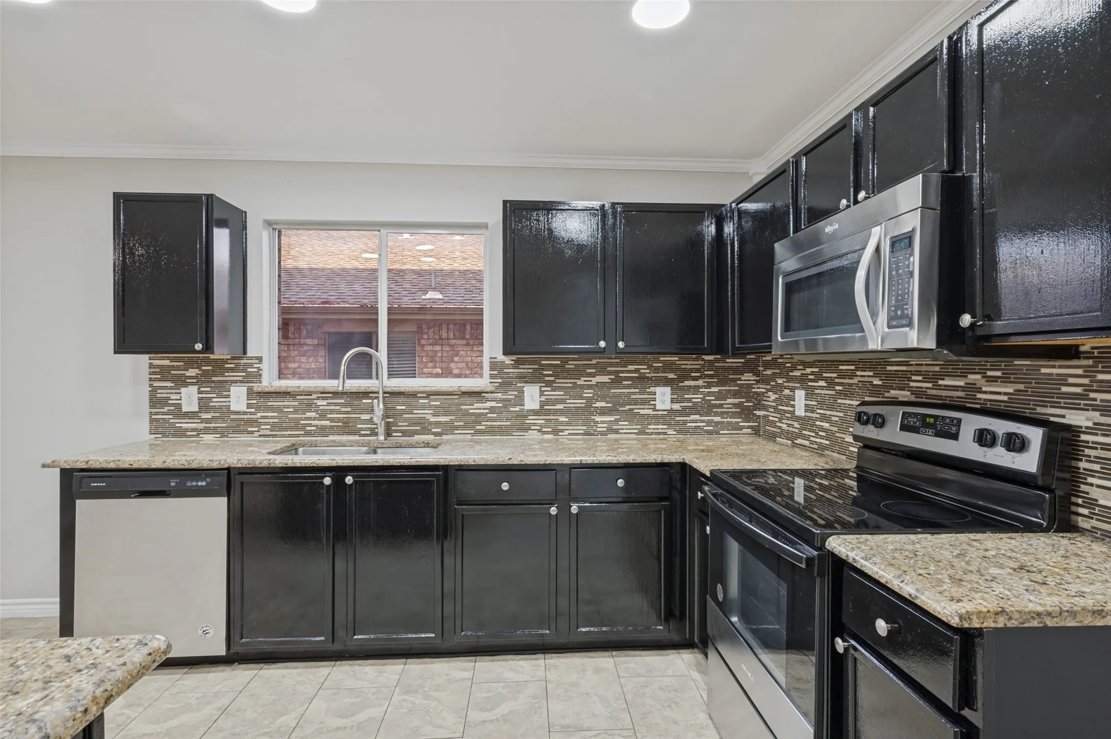 Kitchen featuring dark cabinetry, light-toned countertops, stainless steel appliances, and a mosaic tile backsplash