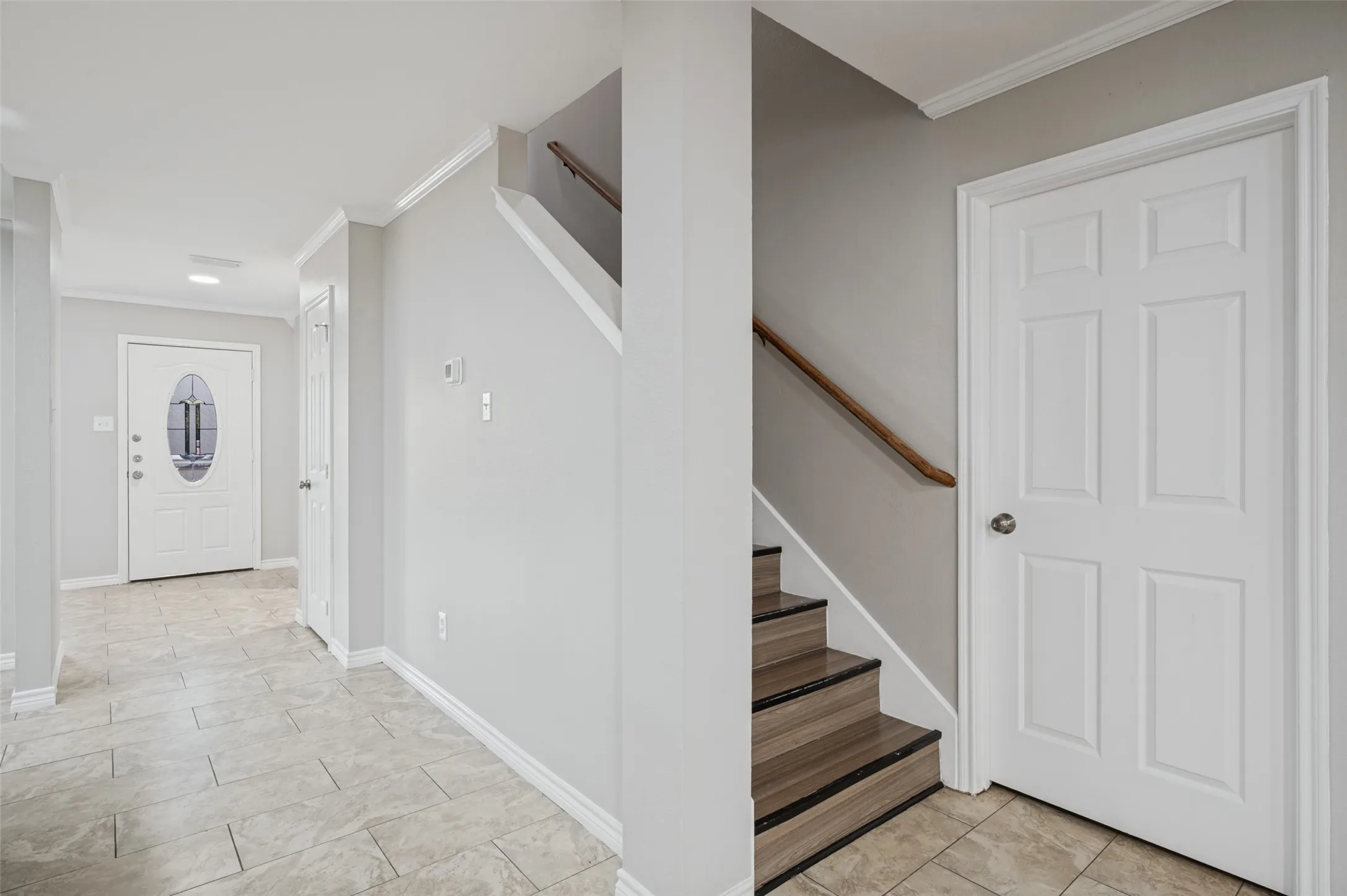 Tile flooring leading to a wood-finish staircase with a wood handrail
