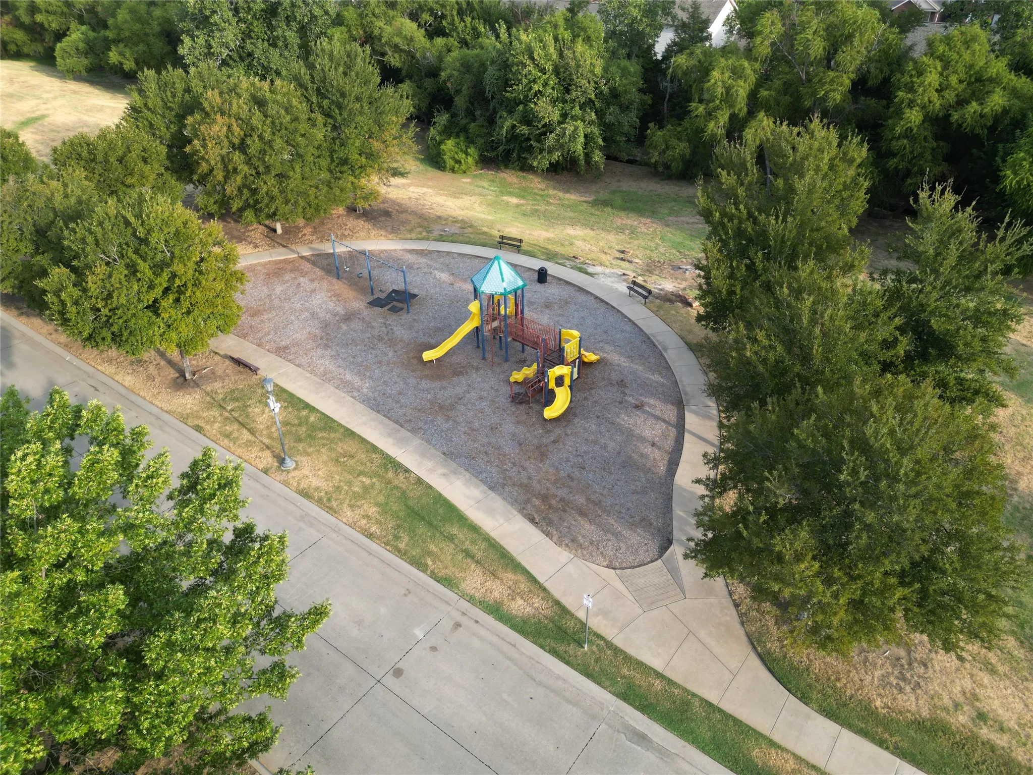 Community playground with a colorful play structure, swings, and a curved paved pathway