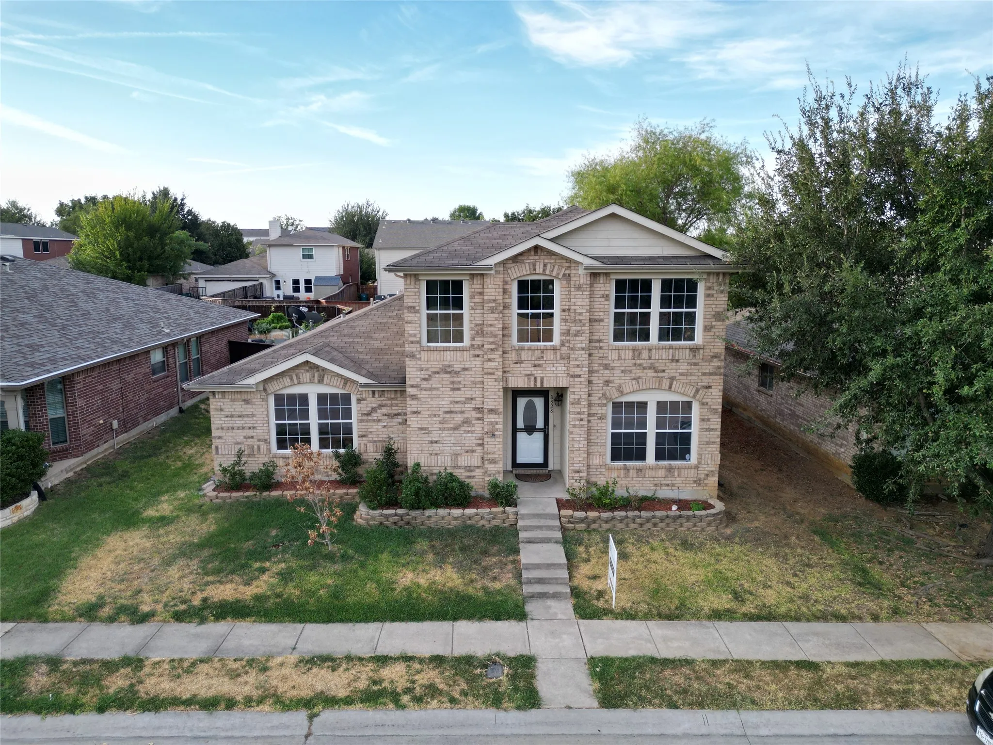 Two-story brick exterior with a gabled roofline, multiple pane windows, and a paved walkway leading to the front entry