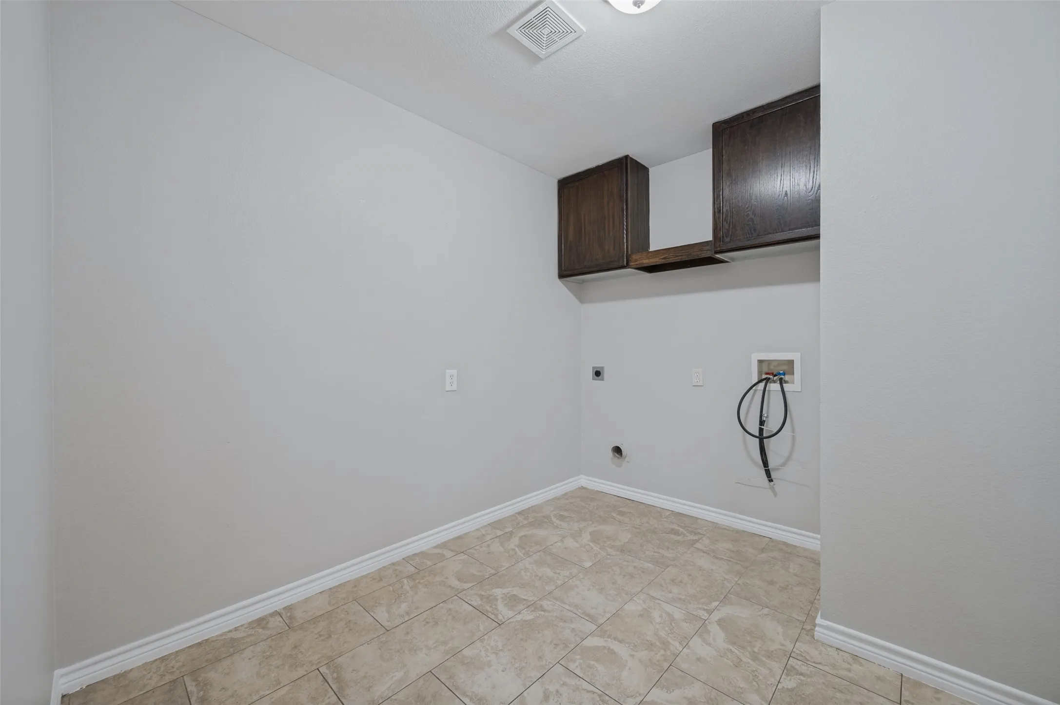 Tile flooring, neutral wall paint, dark wood-finish cabinetry, upper cabinetry, and laundry hookups