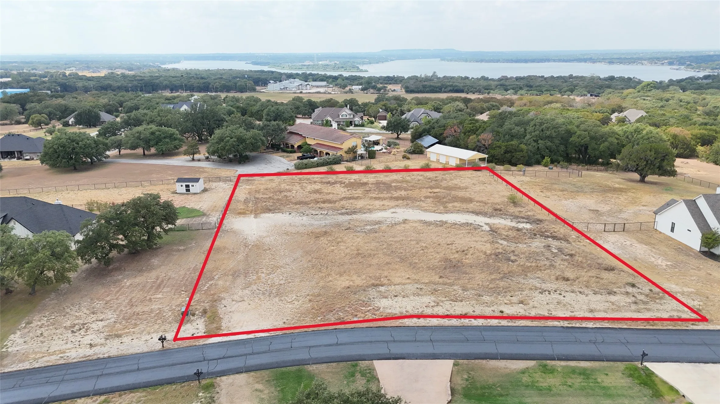 Undeveloped land parcel with a paved road frontage, surrounded by established properties and distant water scenery