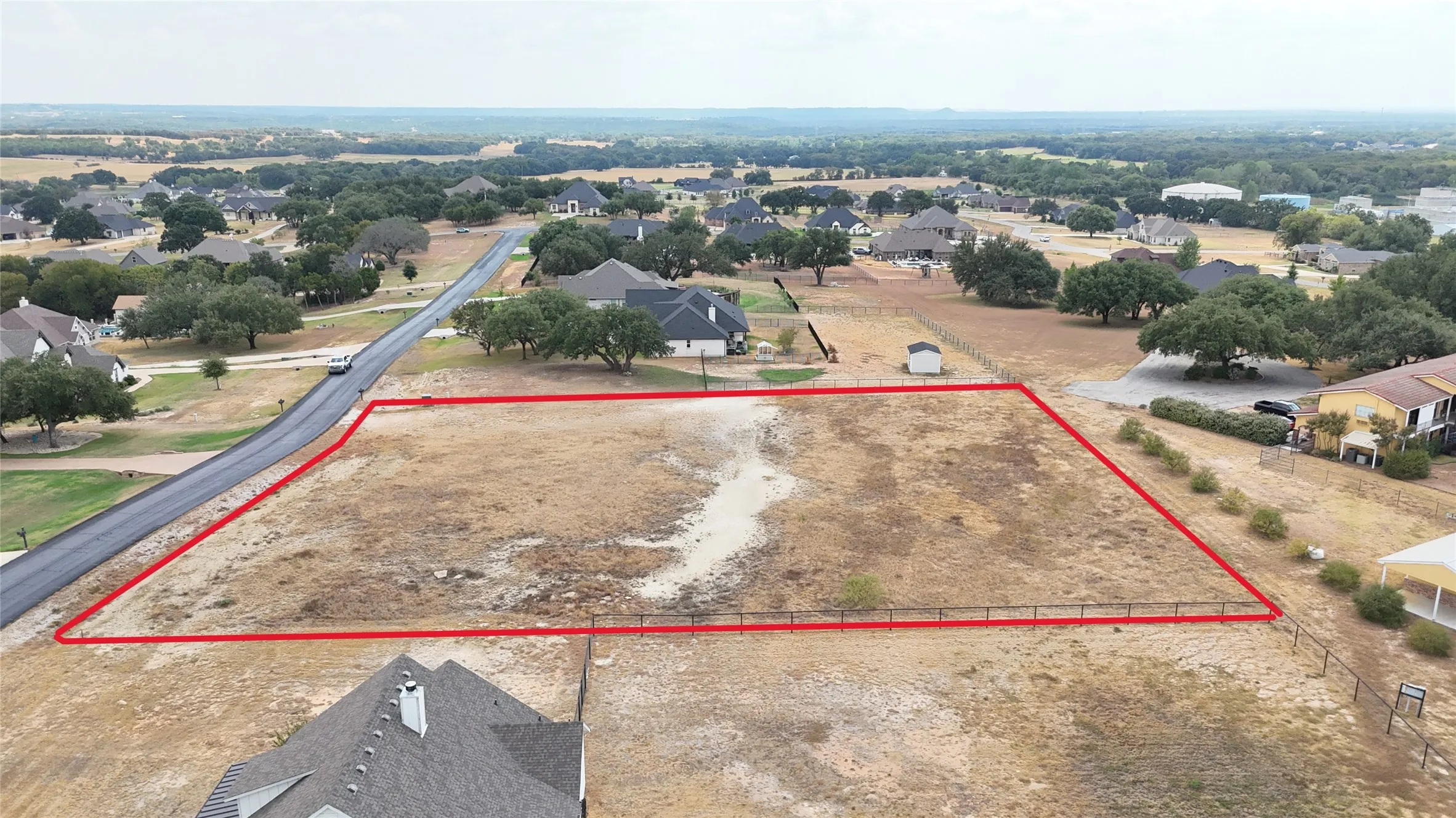 Expansive undeveloped lot featuring a paved road frontage and perimeter fencing on three sides