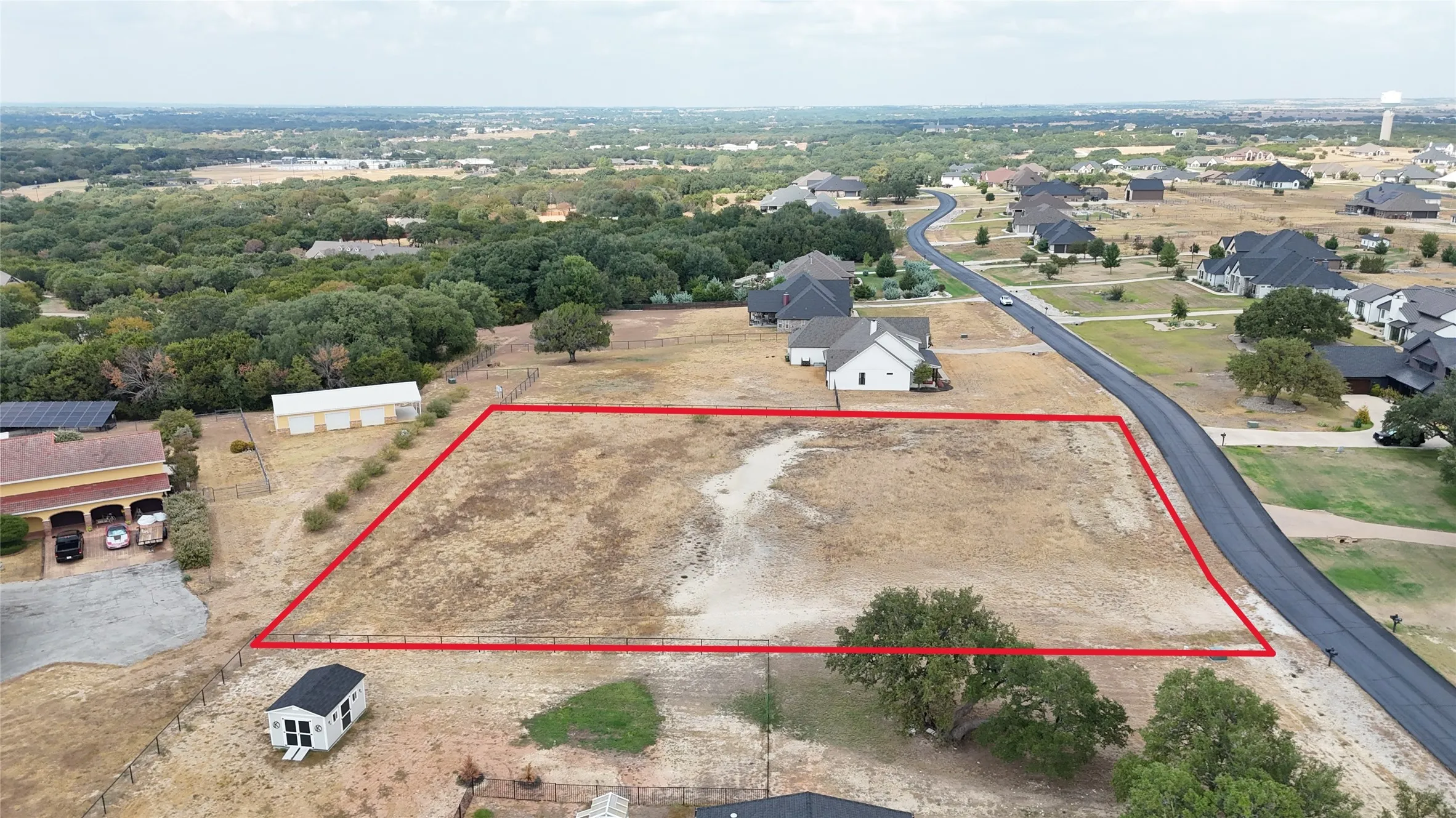 Expansive undeveloped lot with a level grade, surrounded by mature trees and residential properties, featuring direct access to a paved road