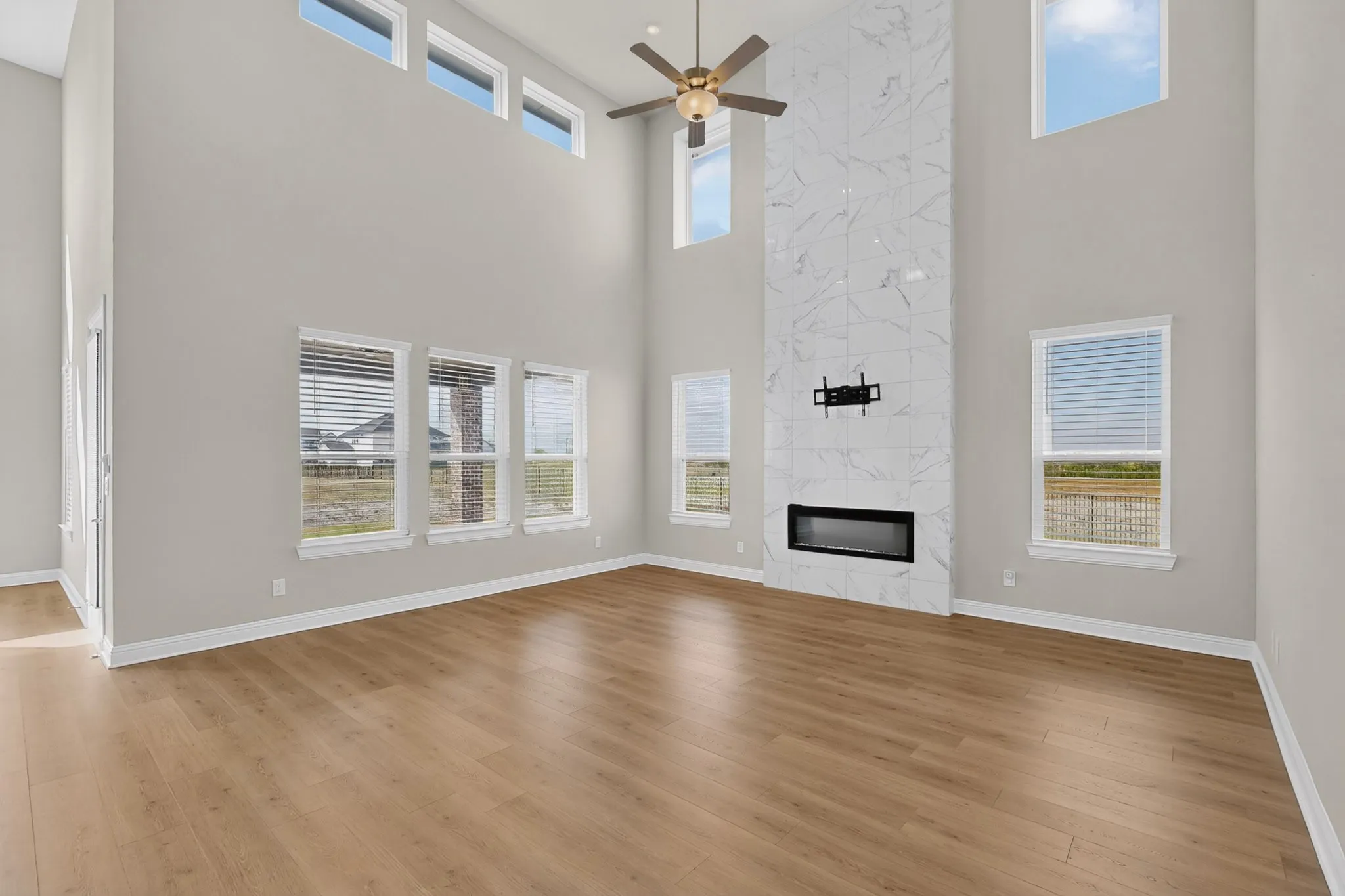 Soaring ceilings, abundant natural light from multiple windows, elegant wood-finish flooring, and a floor-to-ceiling accent wall with an integrated electric fireplace