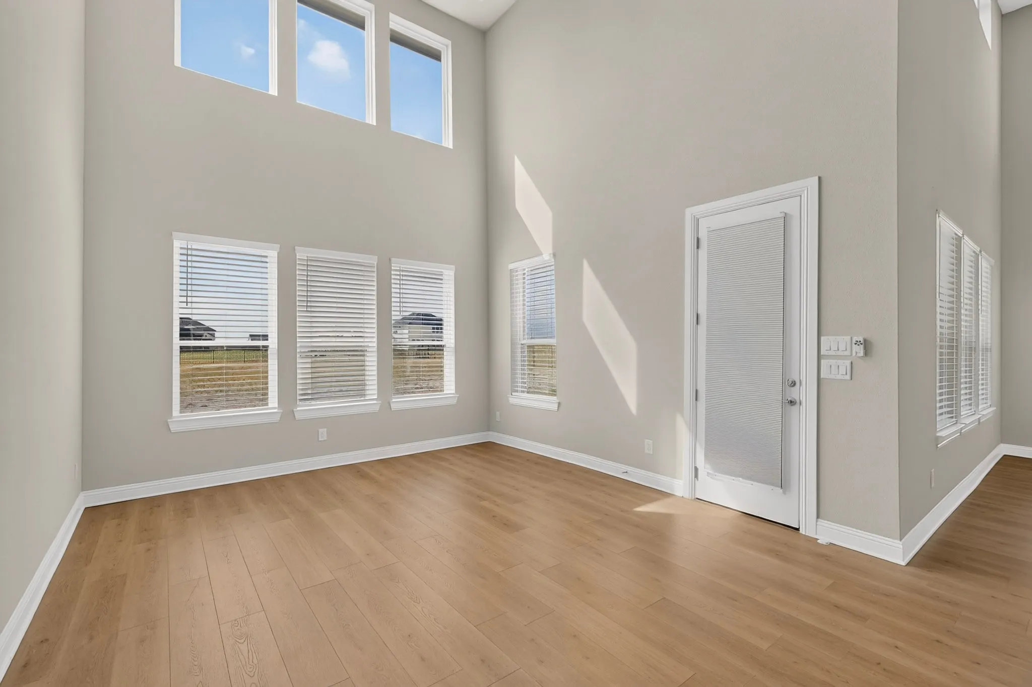 Soaring ceilings, abundant natural light, wood-finish flooring, white trim, and a frosted glass-paneled door
