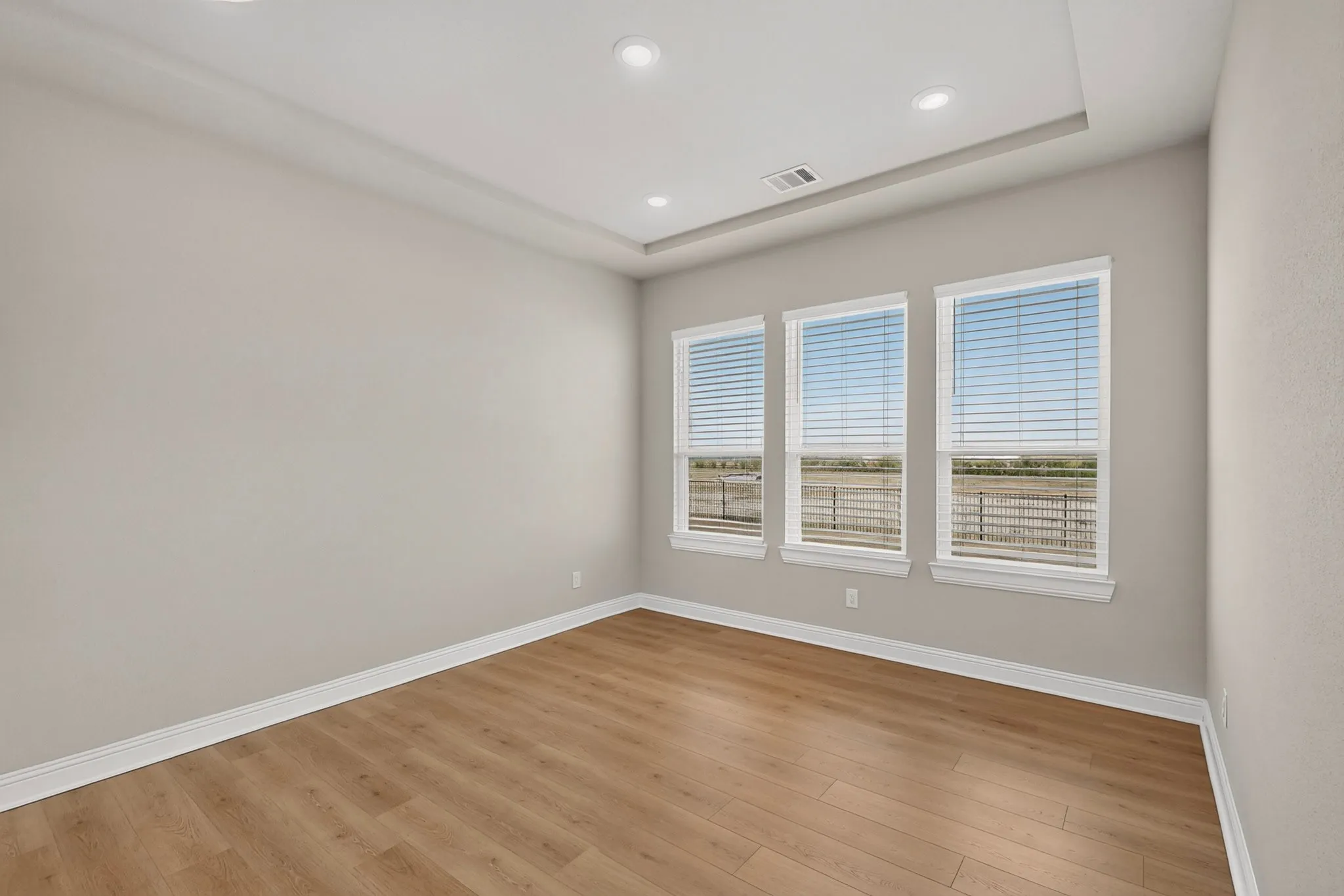 Recessed ceiling lighting, tray ceiling, wood-finish flooring, three windows with blinds, and neutral wall tones