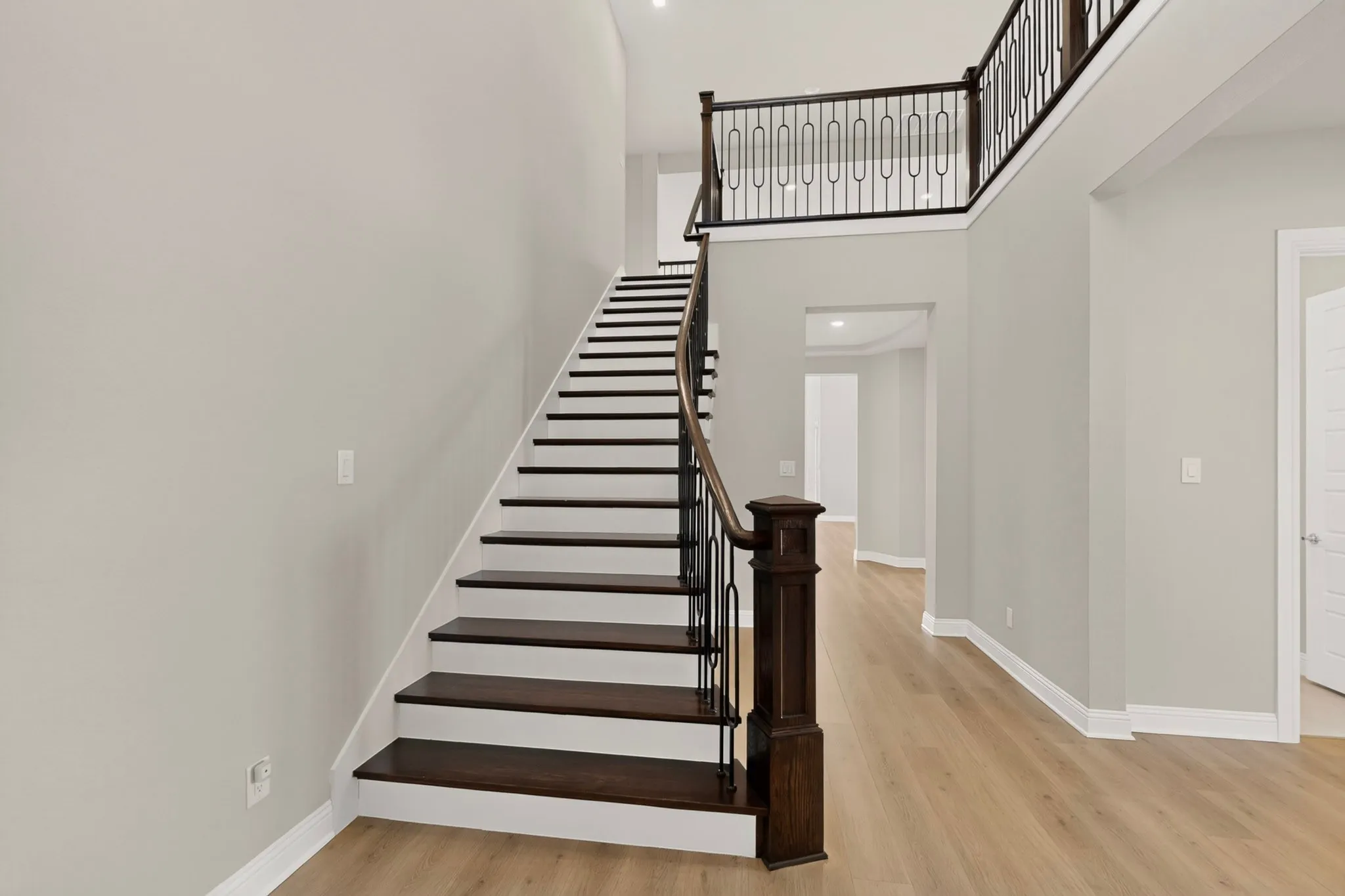 Two-story entry featuring light wood-finish flooring, a dark wood staircase with white risers, and wrought iron balusters with a dark wood handrail