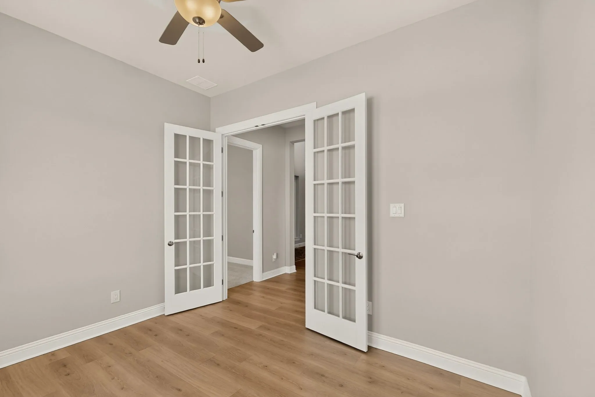 Wood-finish flooring, neutral wall paint, white trim, and a ceiling fan with light fixture