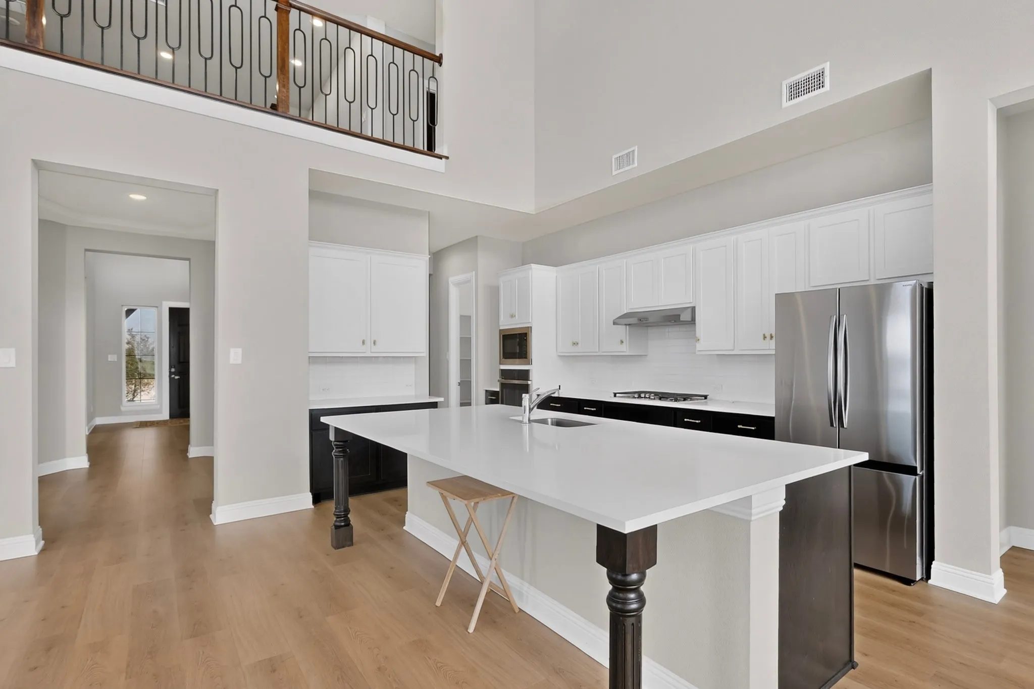 Open-concept kitchen featuring an expansive island with a pristine countertop, white shaker cabinetry, stainless steel appliances, and wood-finish flooring