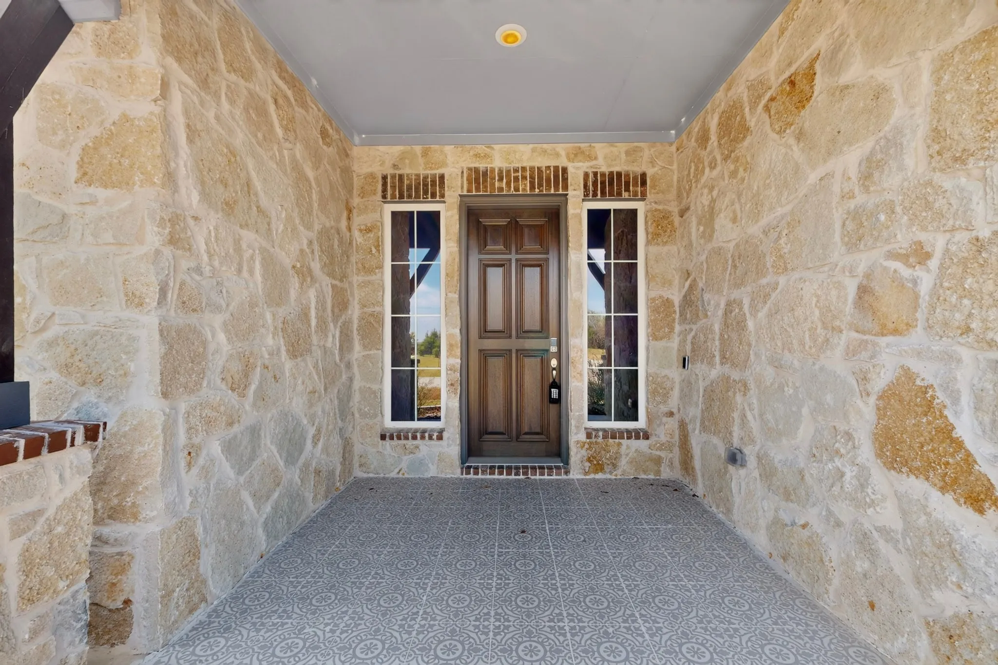 Stone exterior walls featuring a rich wood-panel door with sidelight windows, brick accents, and a patterned tile floor
