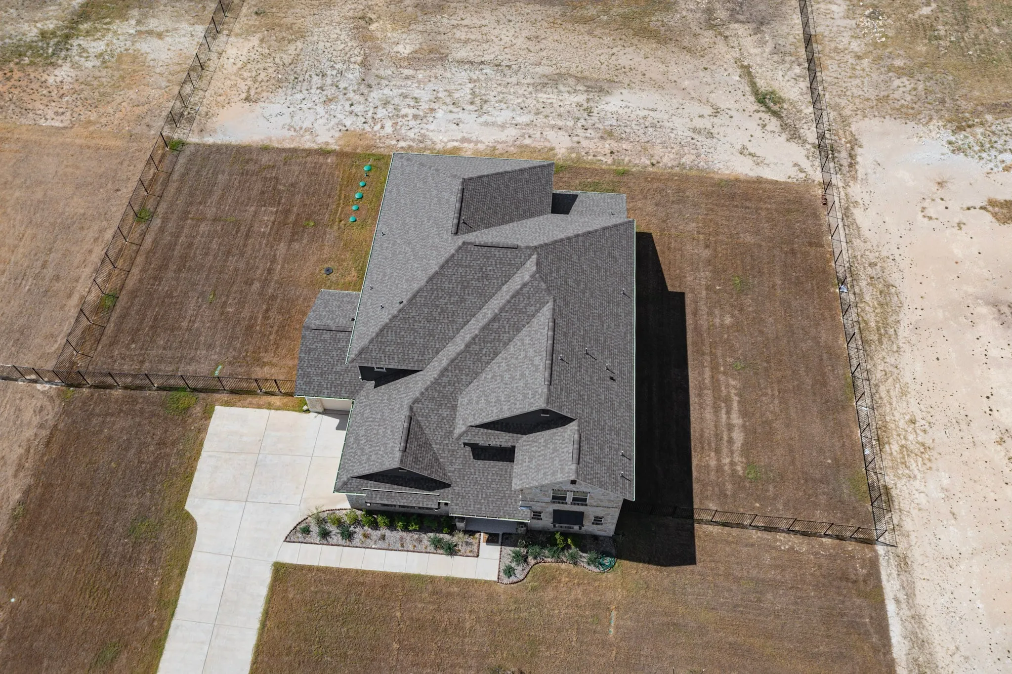 Expansive property featuring a multi-gabled roofline, concrete driveway, and established perimeter fencing