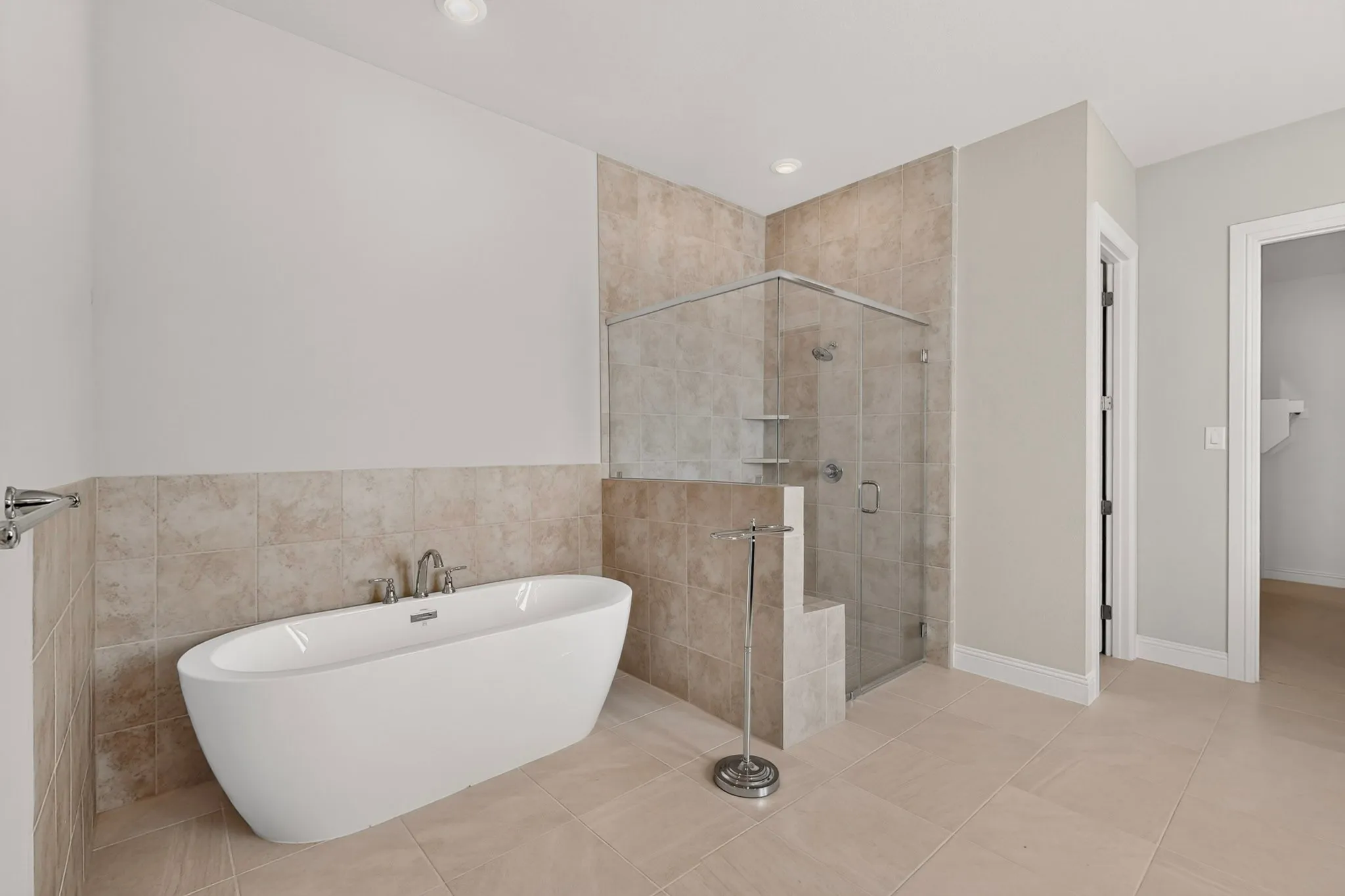 Freestanding soaking tub with chrome fixtures, glass-enclosed shower with tile surround, and large format tile flooring